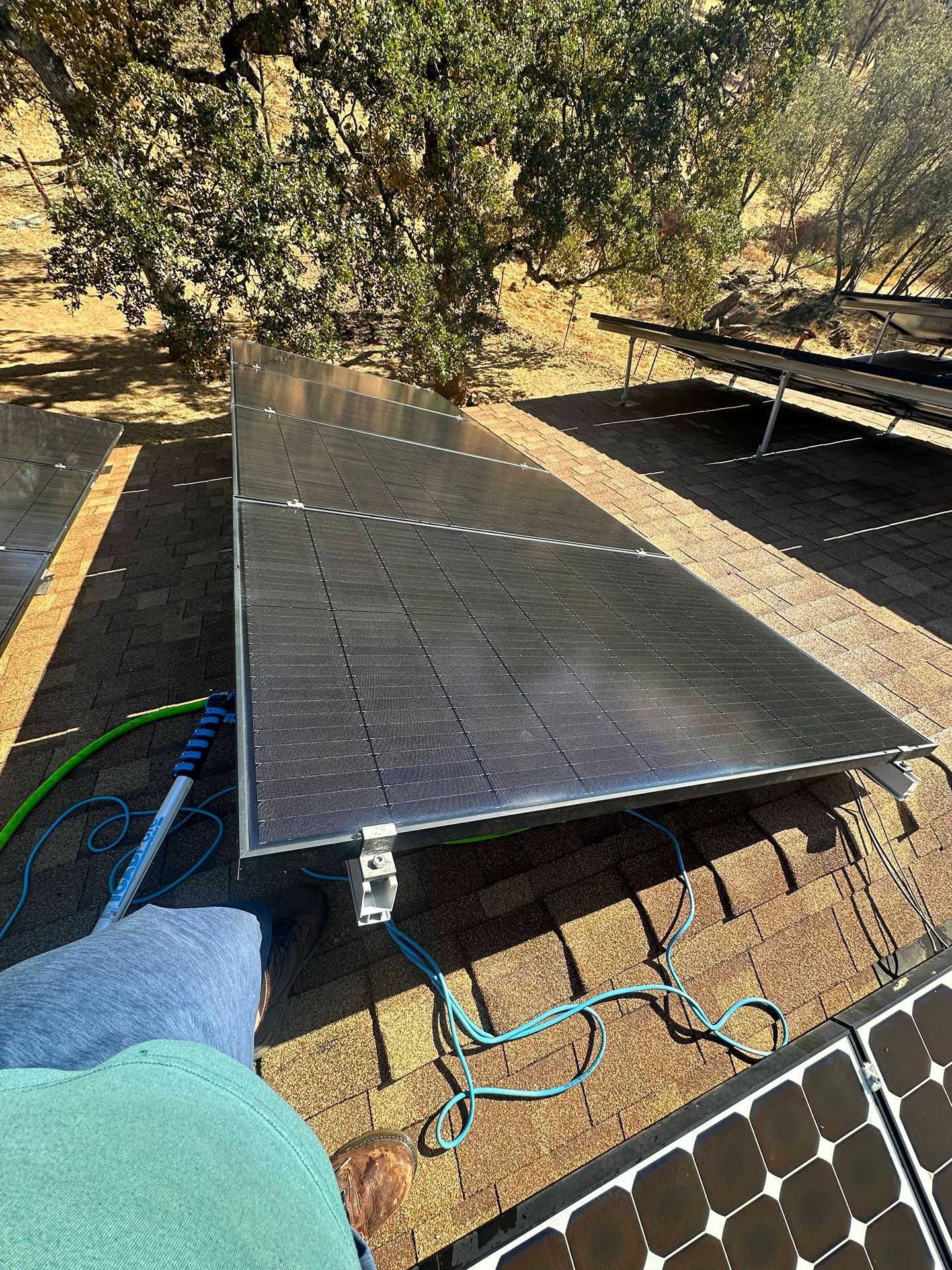 Portable solar panels set up outdoors beside a tree, with cables and equipment on the ground.
