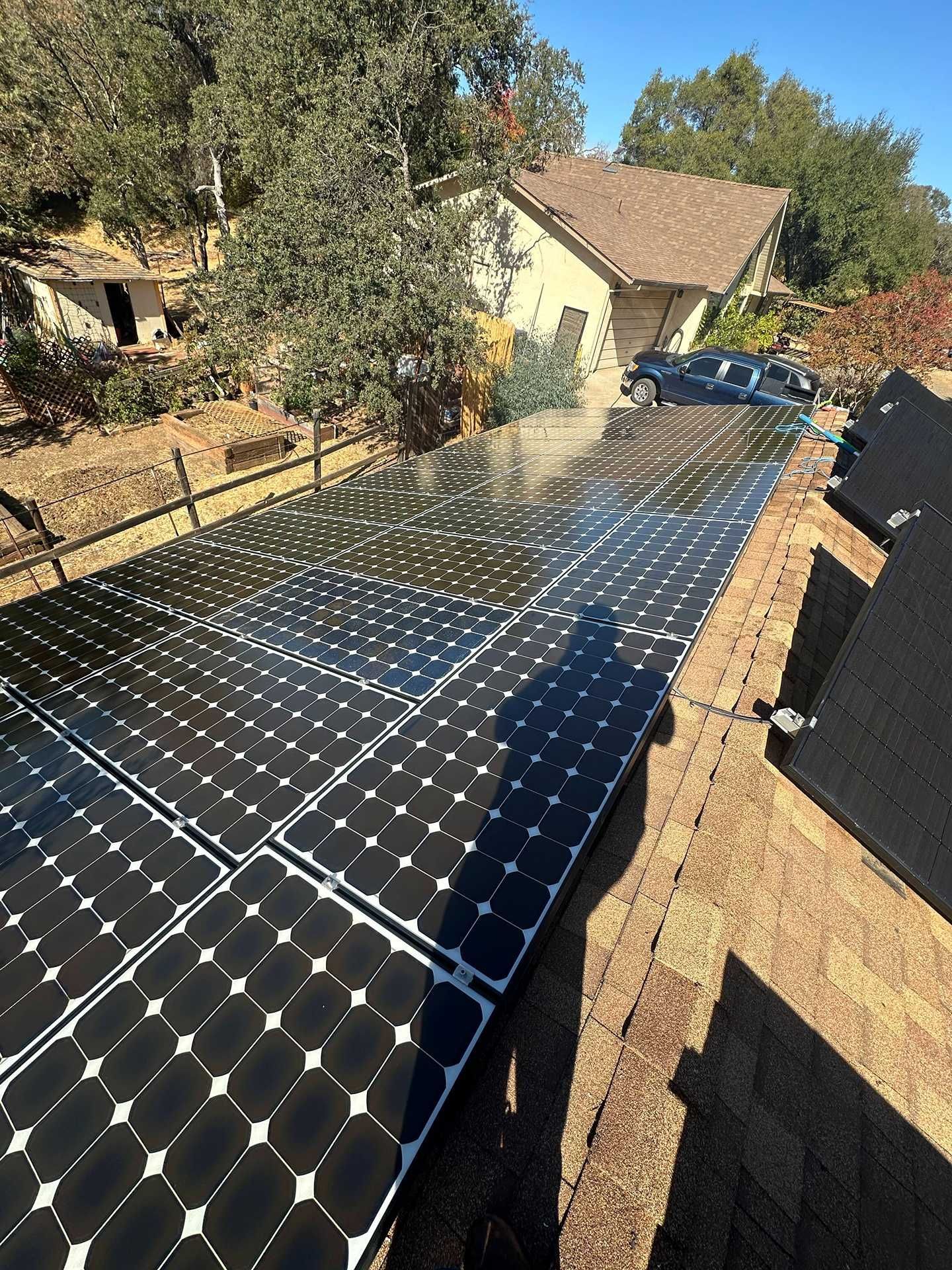Solar panels installed along a sloped driveway beside a house and trees.