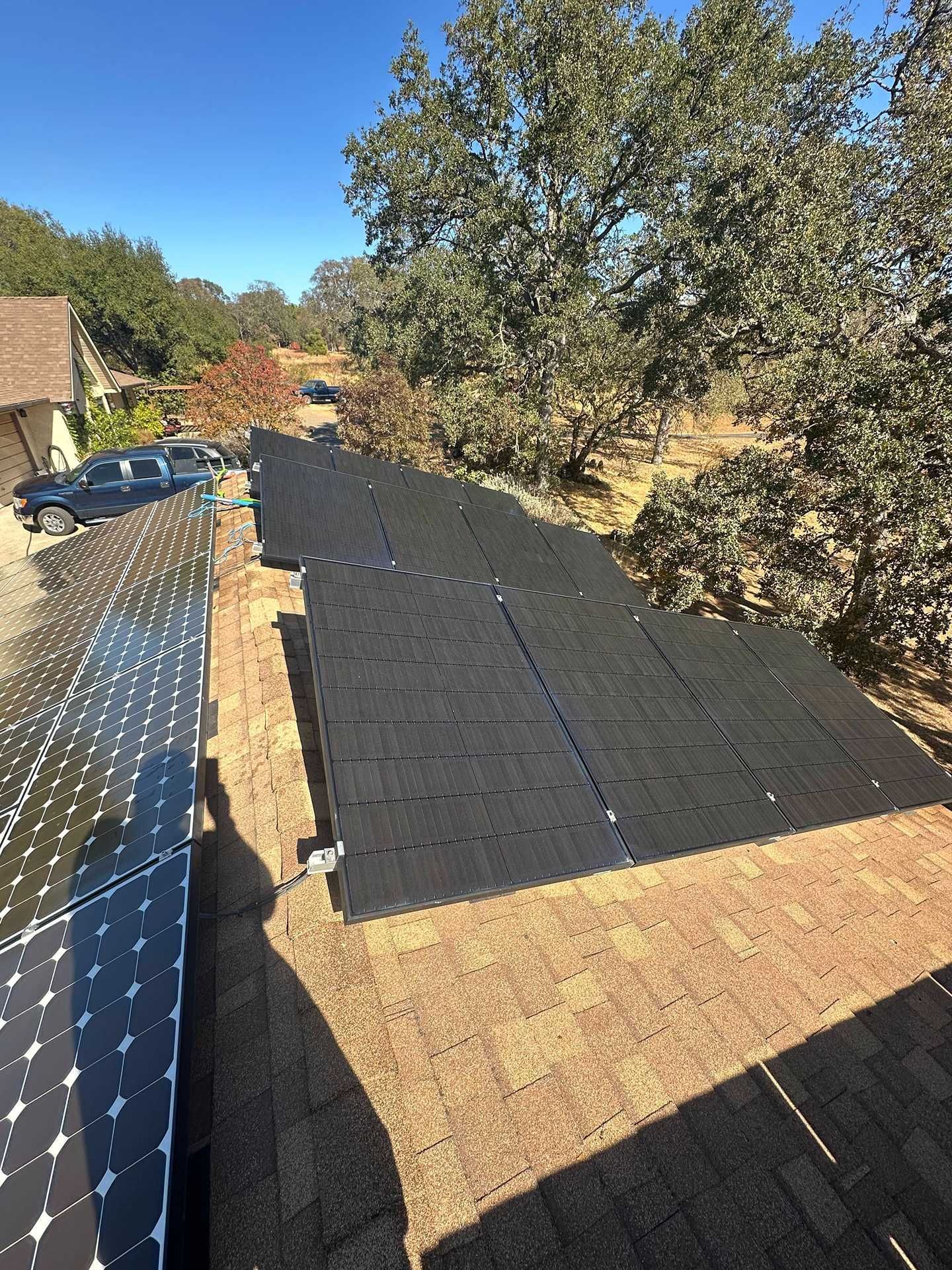 Black solar panels installed on a rooftop with trees and blue sky in the background