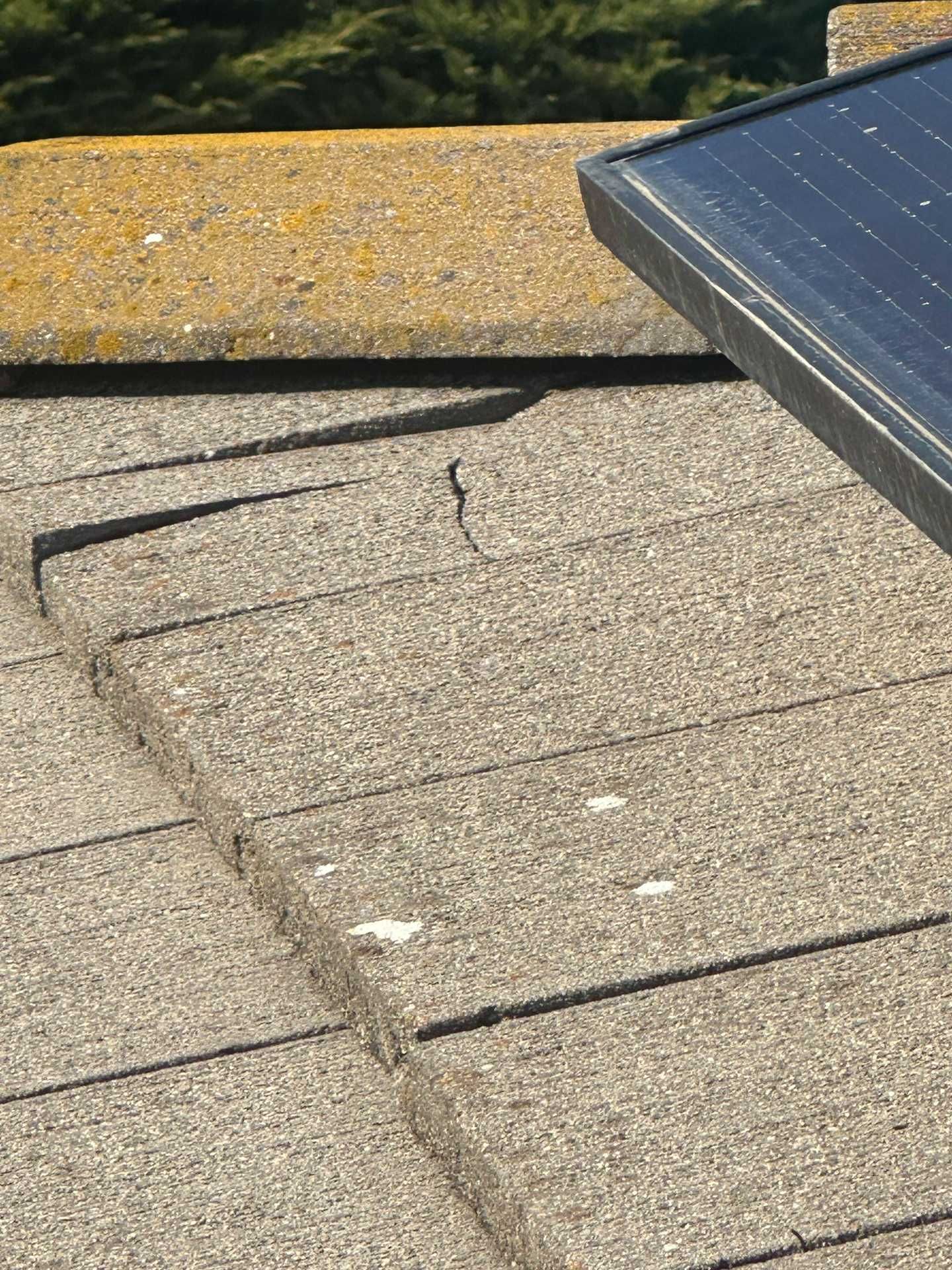Damaged roof shingles around a skylight with a cracked flashing seam.