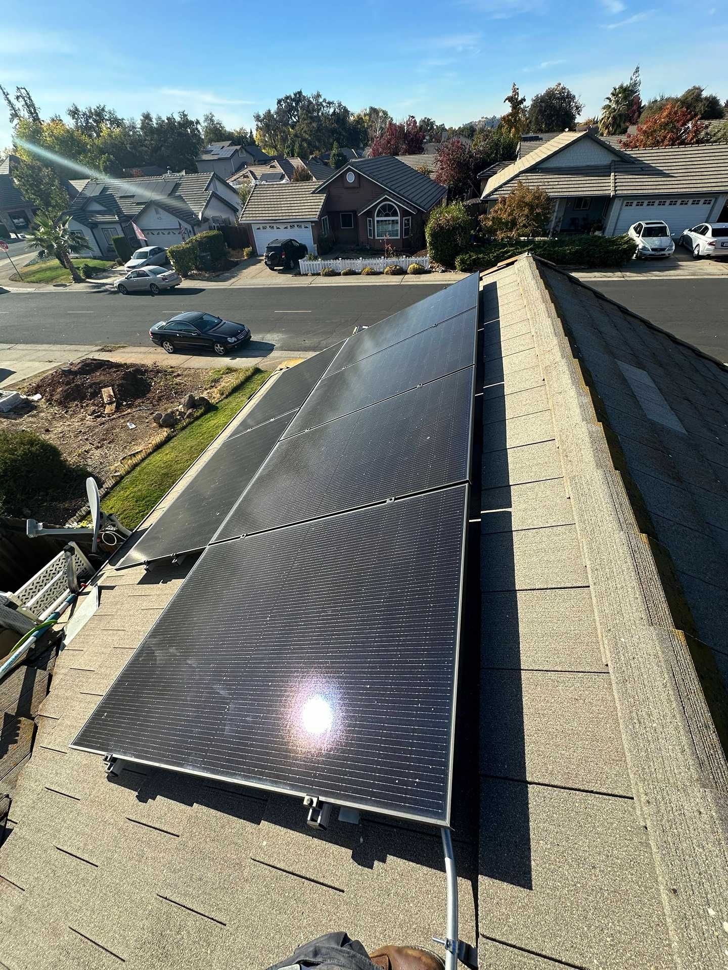 Black solar panel array on a sloped roof in a suburban neighborhood under a clear sky