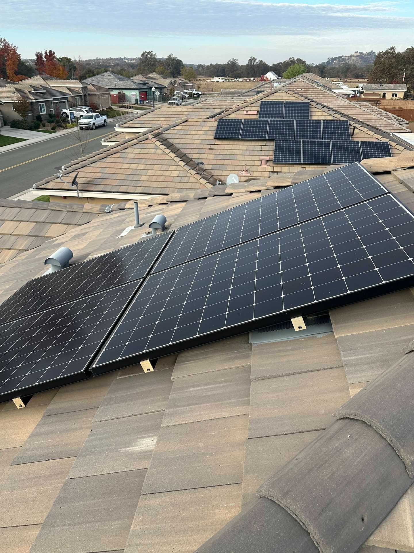 Solar panels installed on a roof in a suburban neighborhood, with rows of houses in the background.