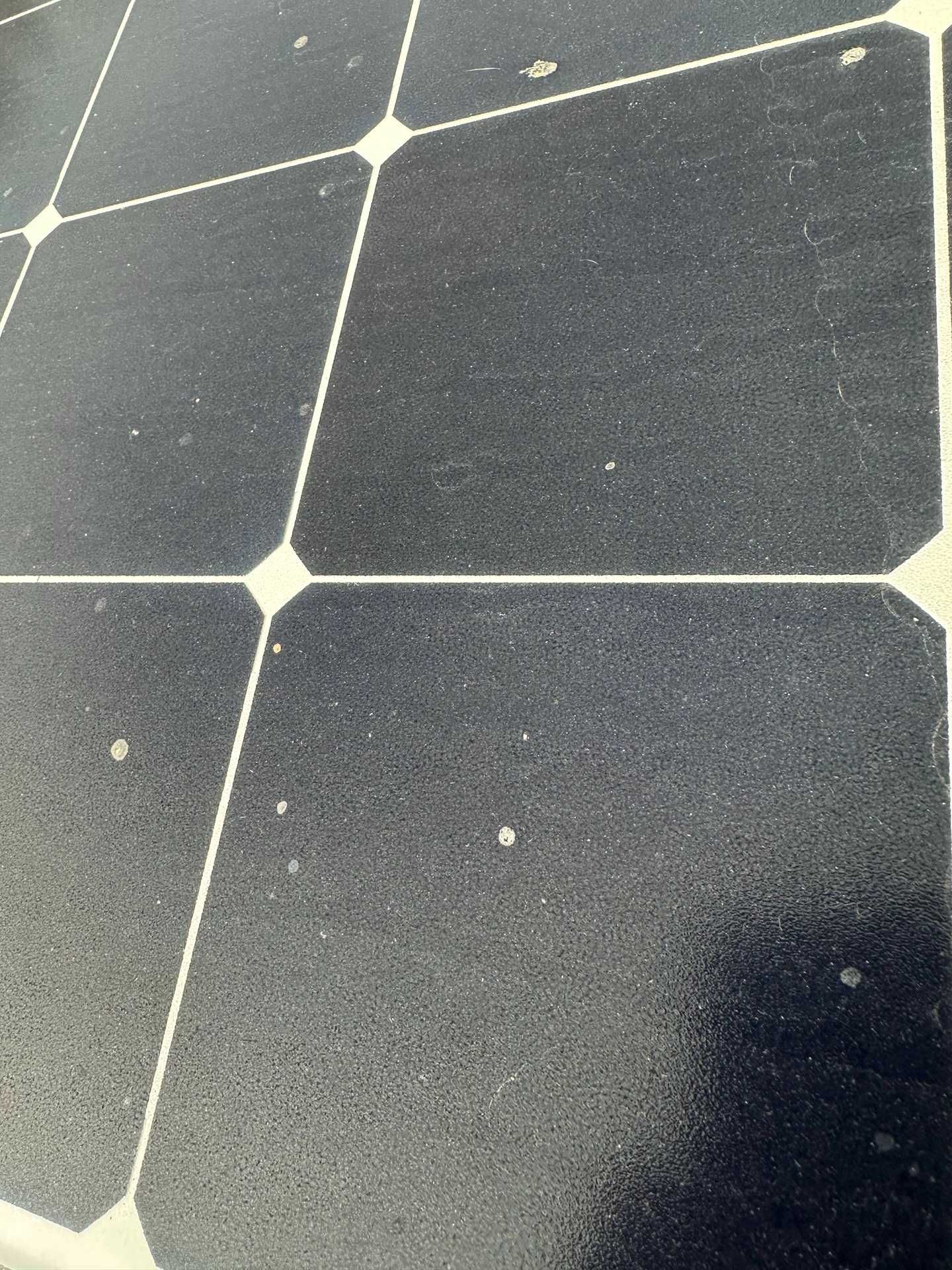 Close-up of dark solar panels with light grid lines and dust speckles.