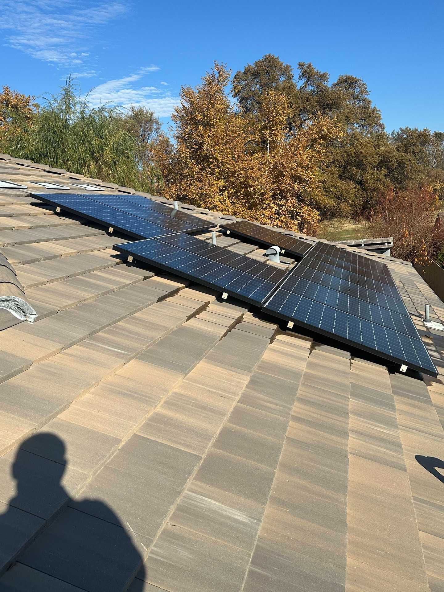 Solar panels mounted on a tiled roof under a blue sky, with autumn trees in the background.