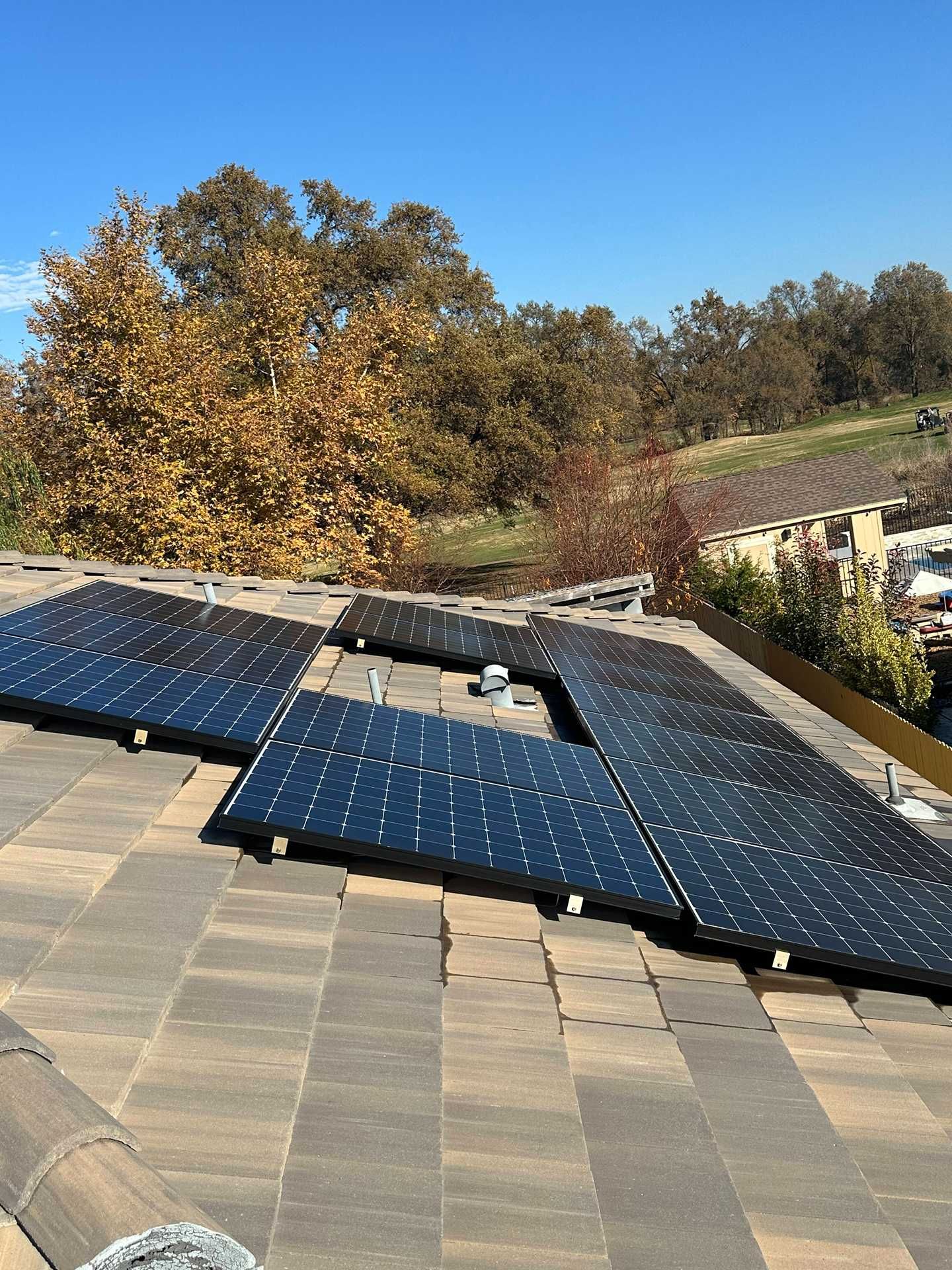 Solar panels on a shingled roof under a clear blue sky, with autumn trees in the background.