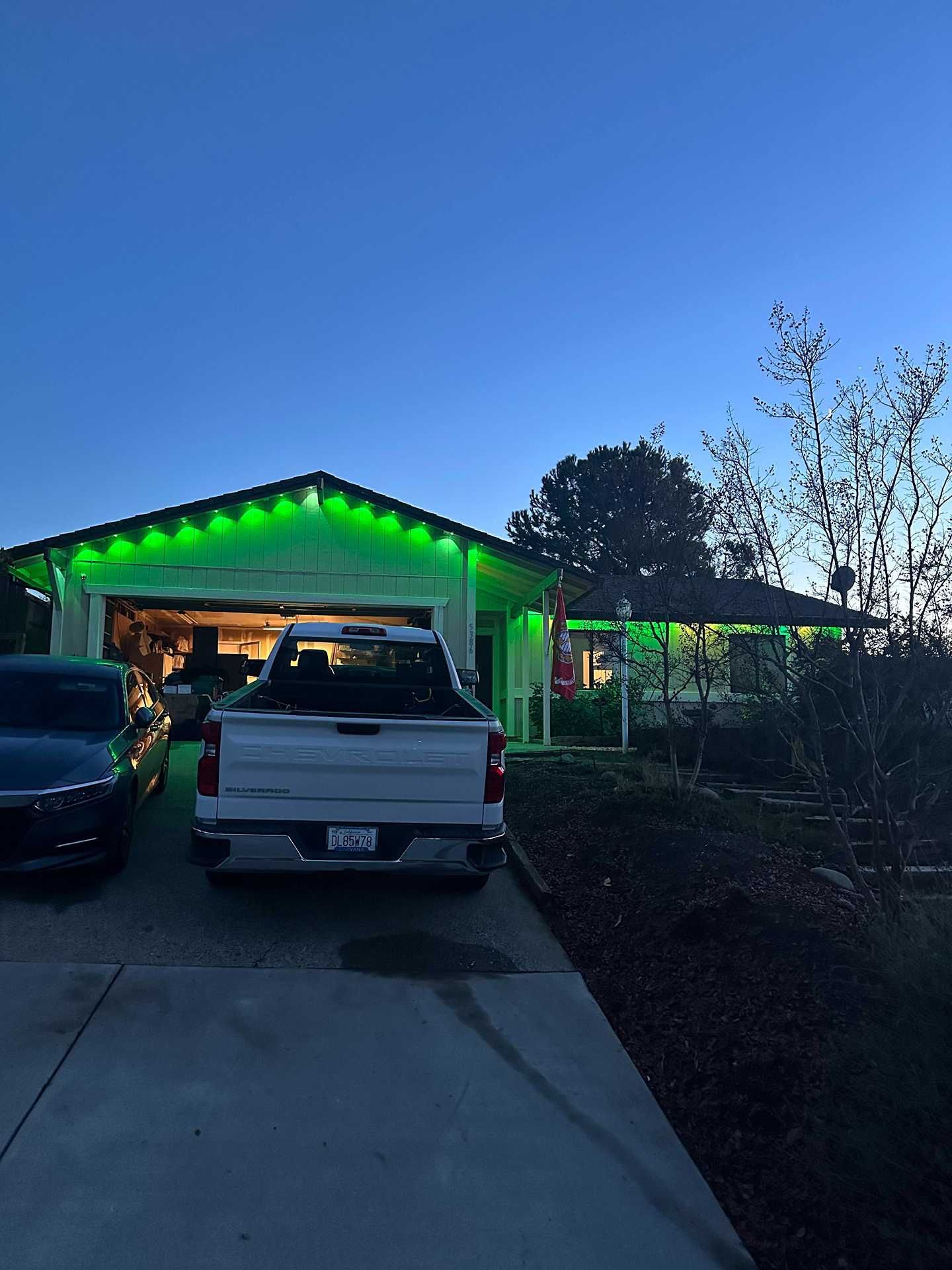 Truck parked in a driveway beside a house glowing with green lights at dusk