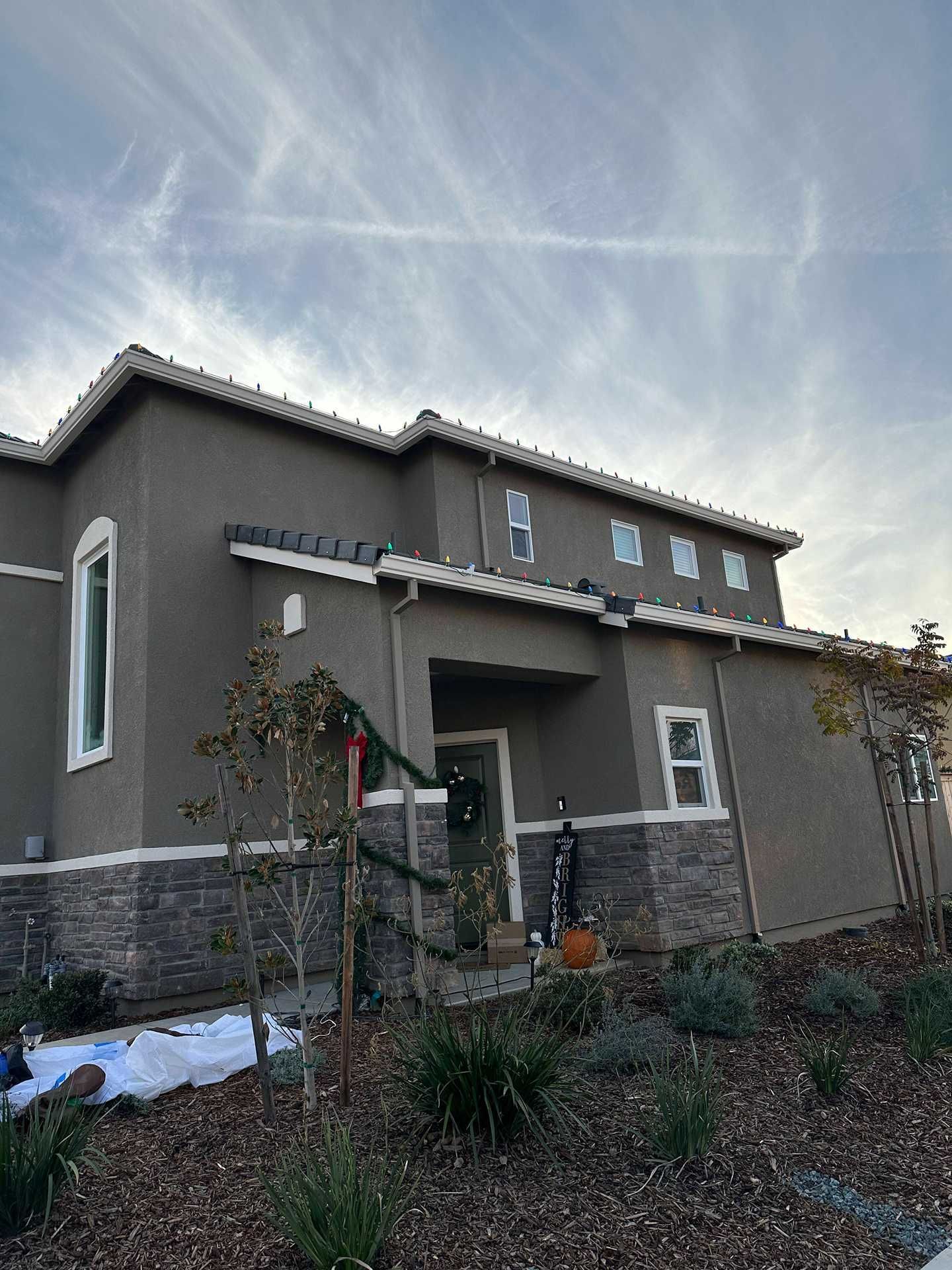 Gray two-story house with a front porch, desert landscaping, and a cloudy sky at sunset