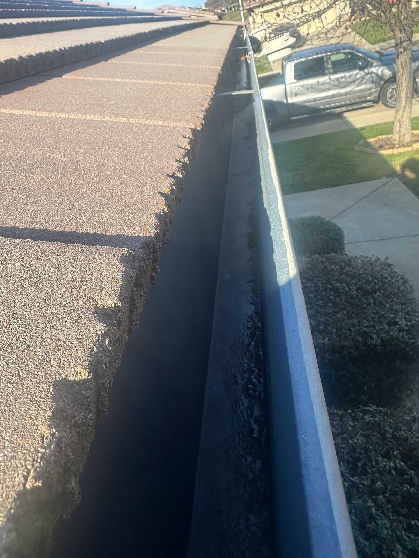 Rooftop view of a gutter along a roof edge beside a sidewalk and shrubs below