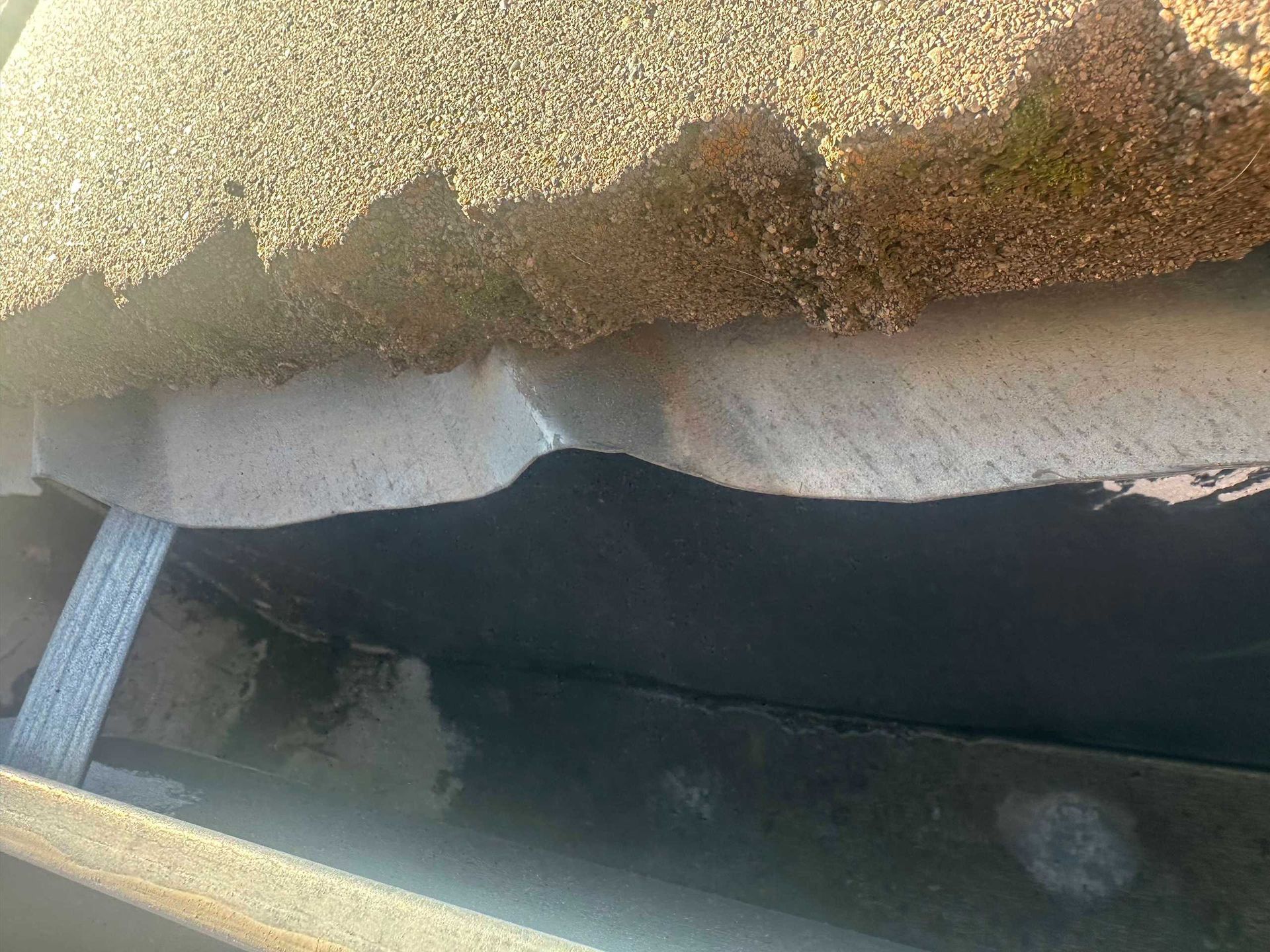 Open wall cavity with dark interior beneath a rough concrete ledge and stucco exterior