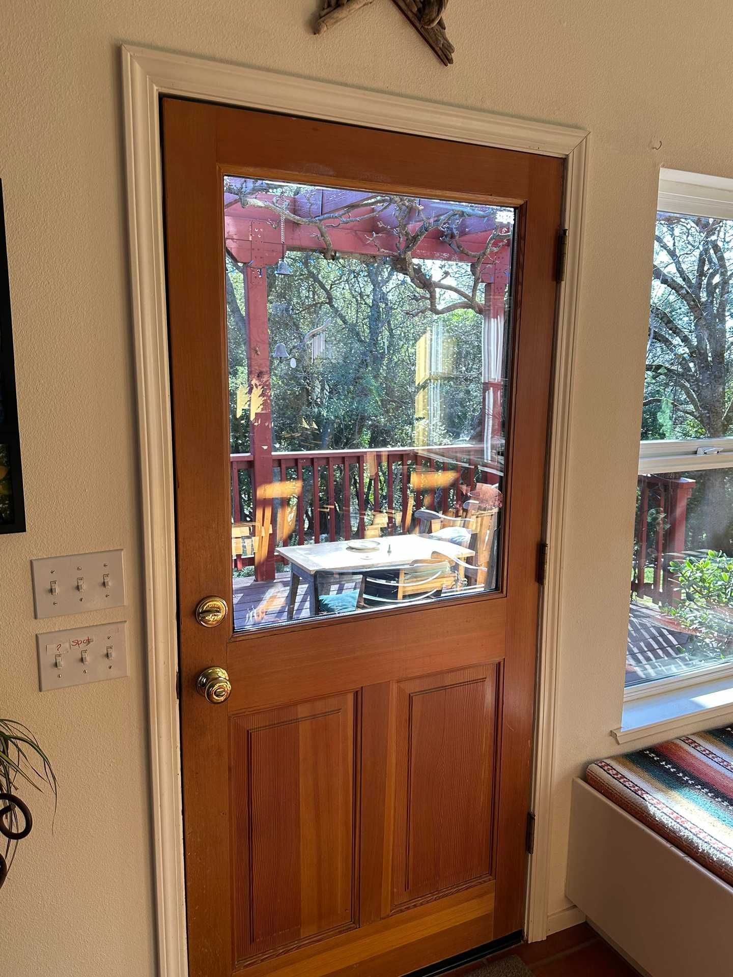 Wooden glass-paneled door opening to a deck with red railing and trees outside