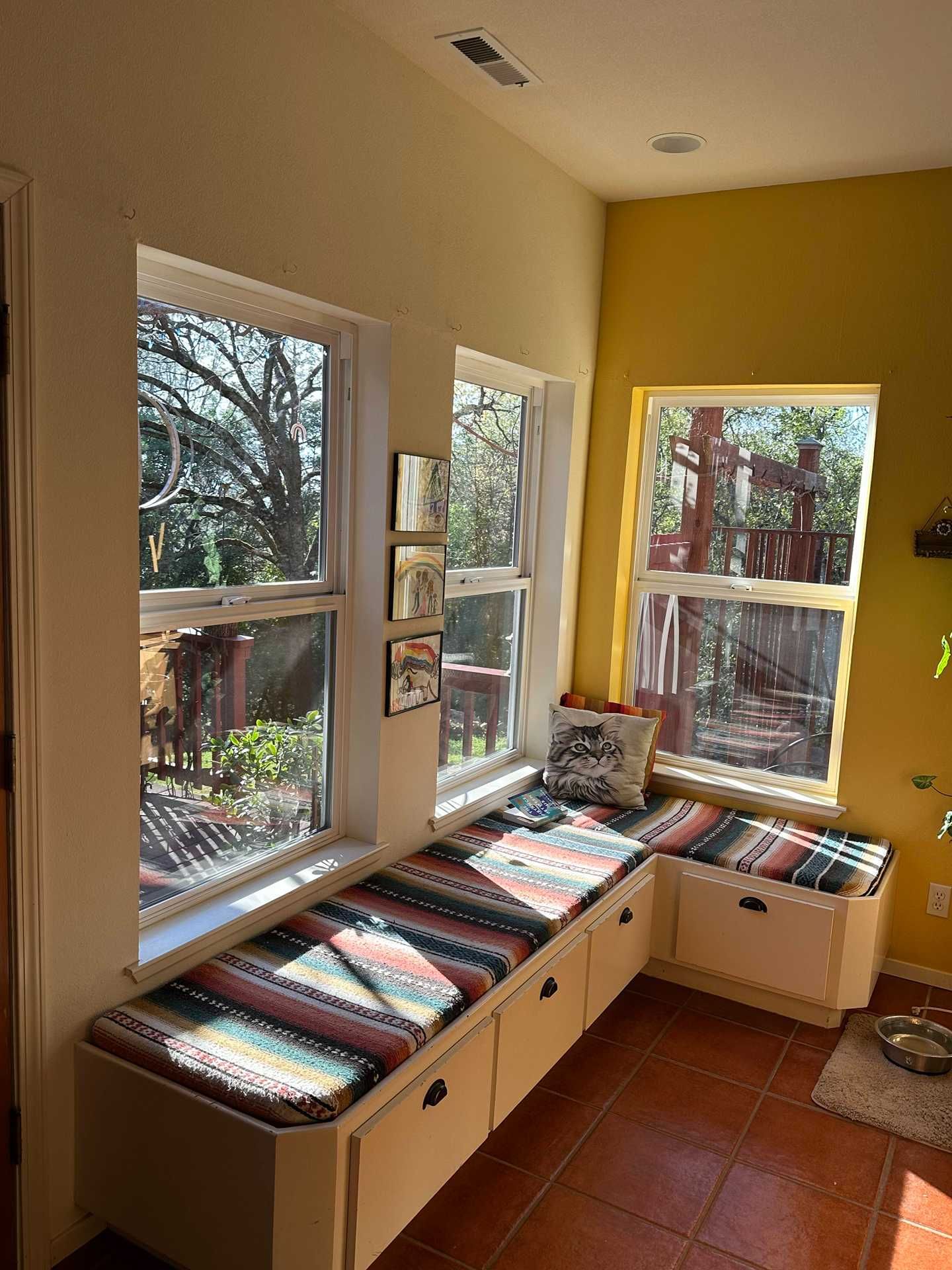 Sunlit corner bench with colorful cushions beneath tall windows in a bright room
