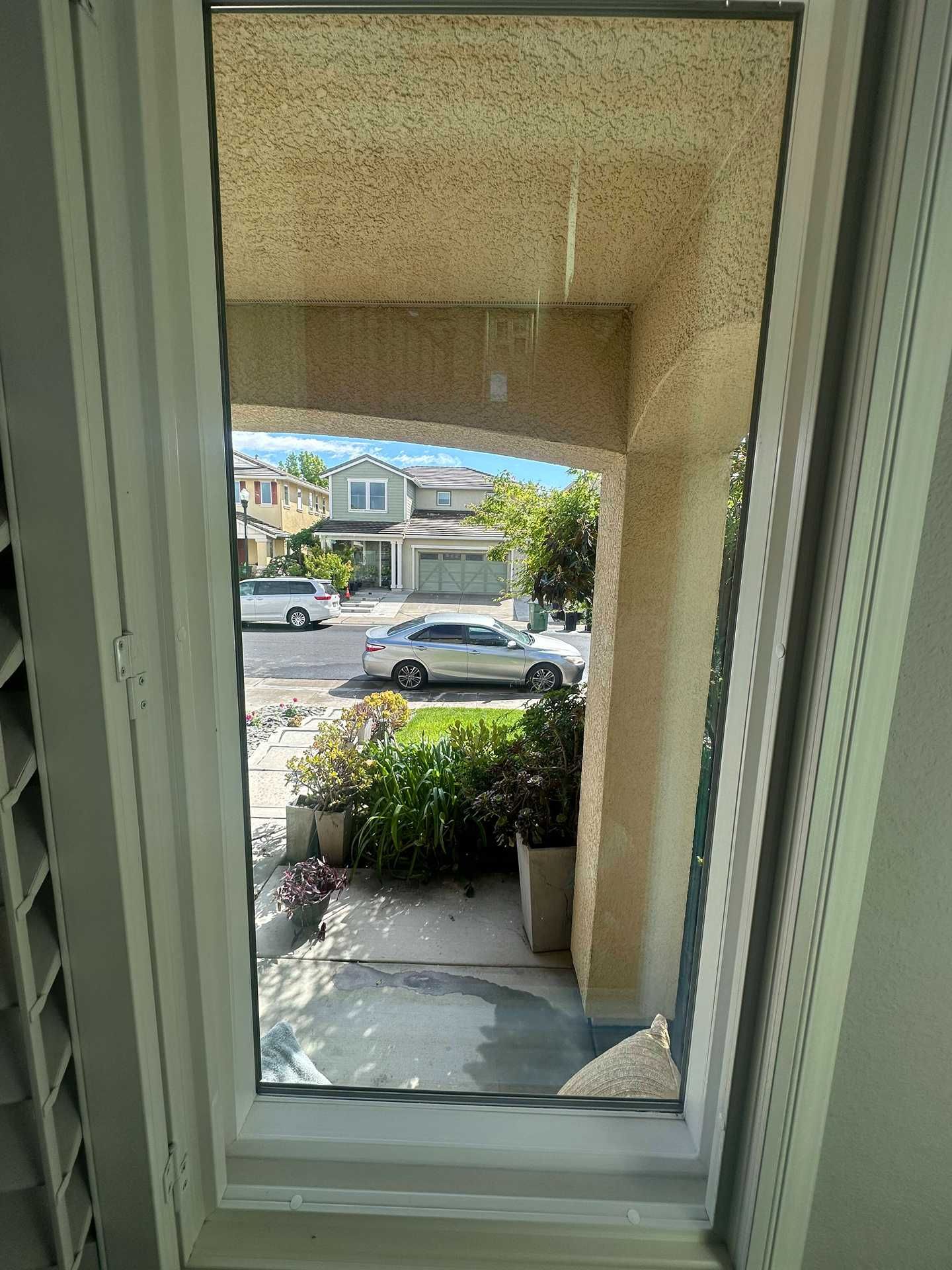 View through a white-framed window to a front porch, sidewalk, parked cars, and houses across the street.