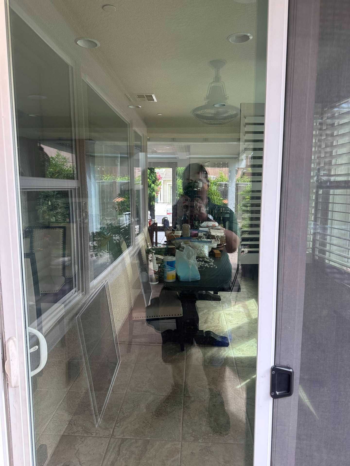 Person standing in a glass door doorway, reflected in the windowed porch hallway.