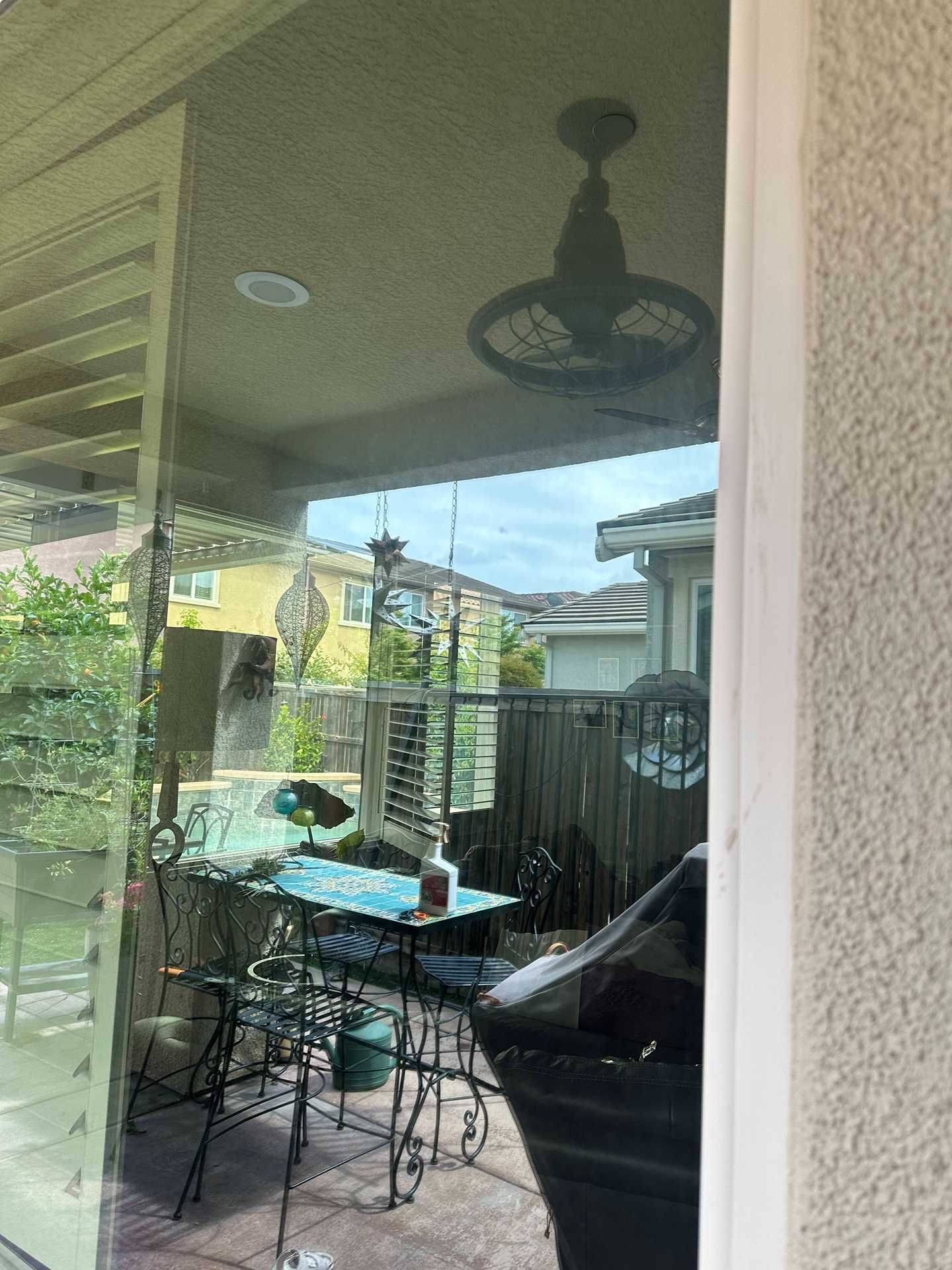 Patio with glass table and chairs, reflected in a sliding glass door under a covered roof.