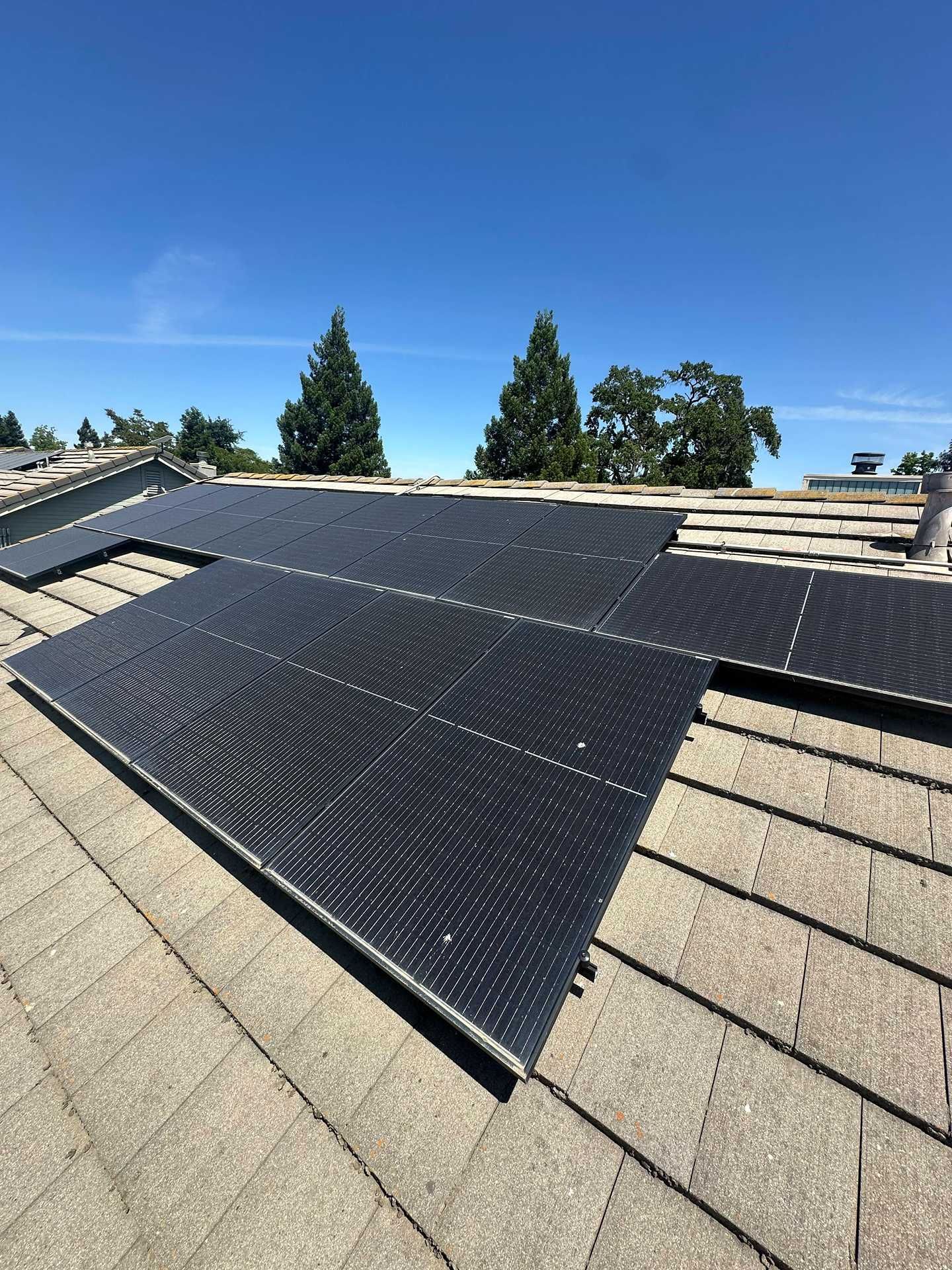 Solar panels installed on a shingled roof under a clear blue sky.