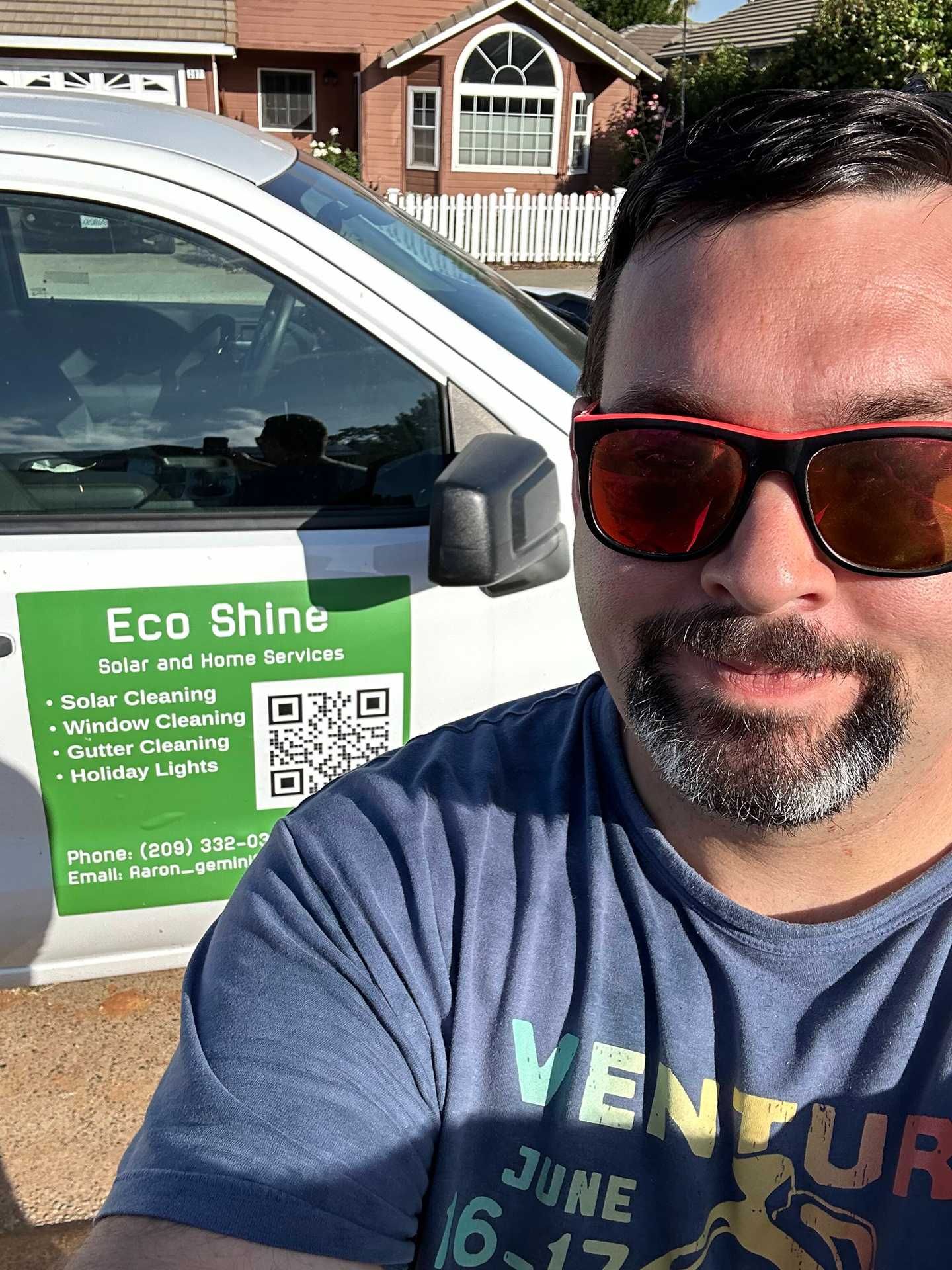 Man smiling in sunglasses beside a white car with an Eco Shine sign at a driveway