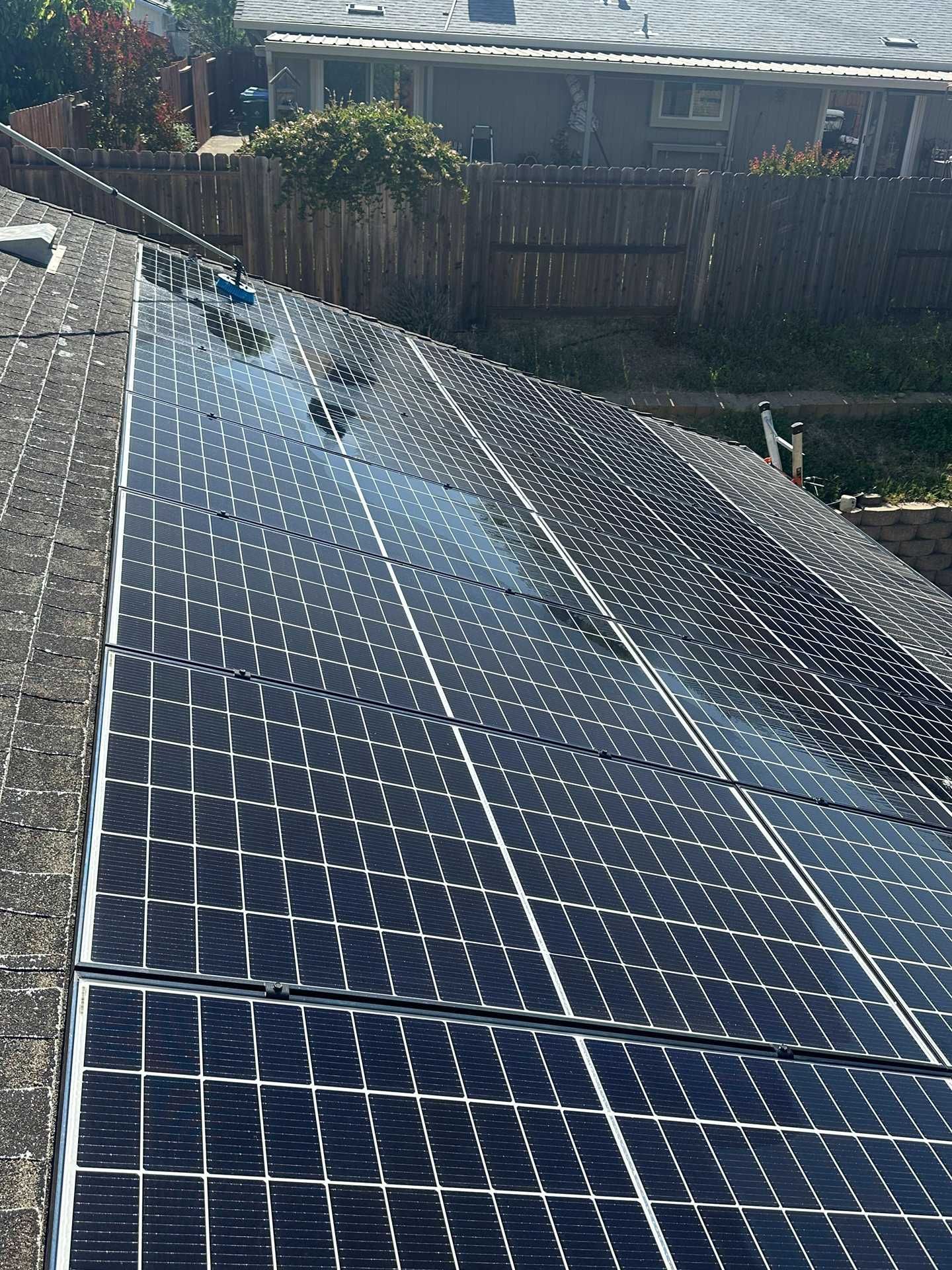 Solar panels installed on a sloped roof, viewed from above with nearby trees and a wooden fence.