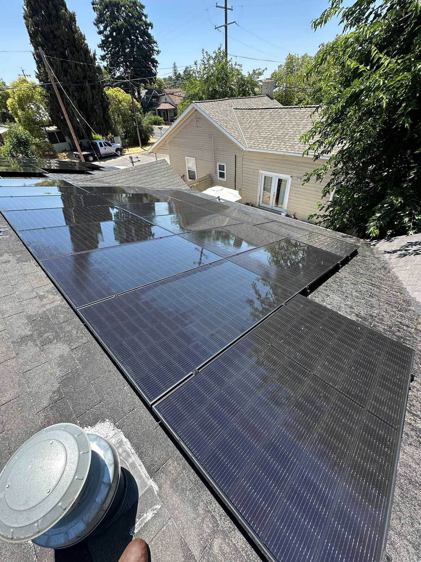 Solar panels on a rooftop beside a beige house under a clear sky.