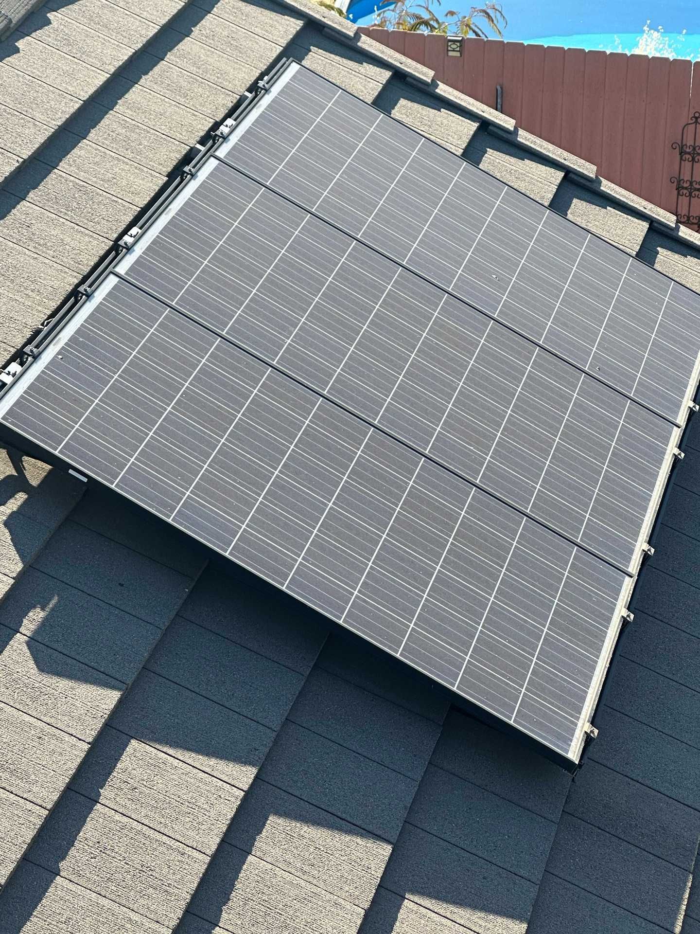 Solar panels installed on a sloped roof with dark gray shingles and a red roof section in the background.