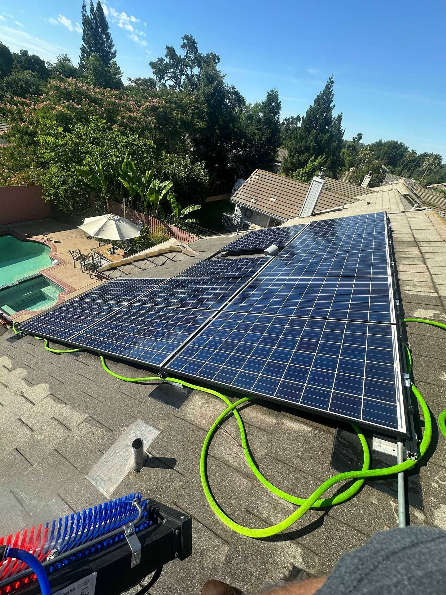 Solar panels laid on a rooftop under repair, with green hoses and tools in a sunny backyard.