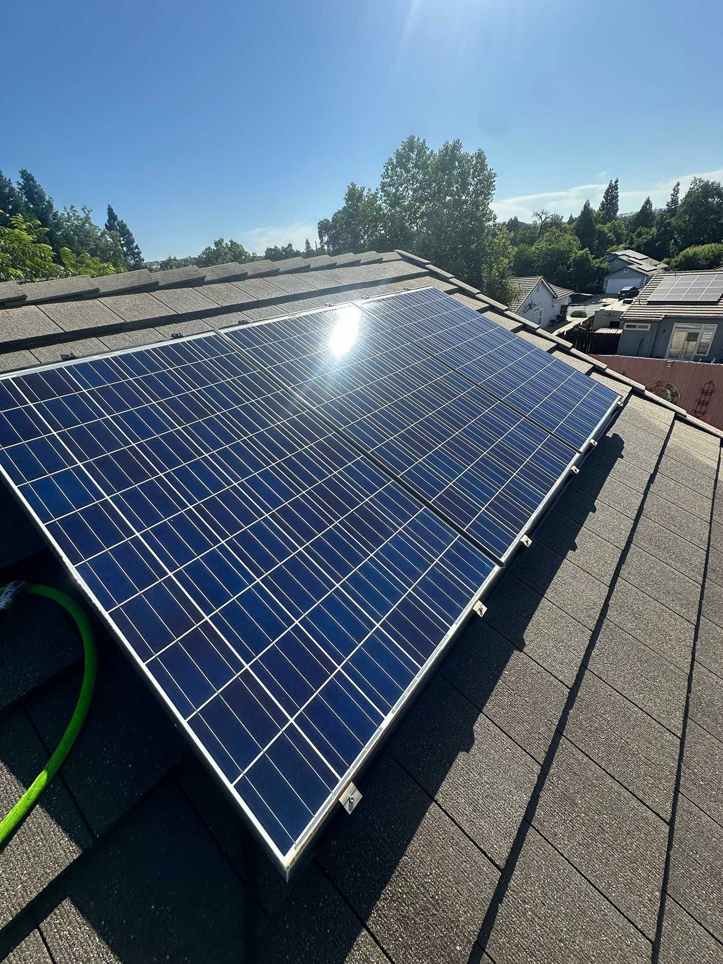 Solar panels on a shingled rooftop under a clear blue sky, with sunlight reflecting off the panels.