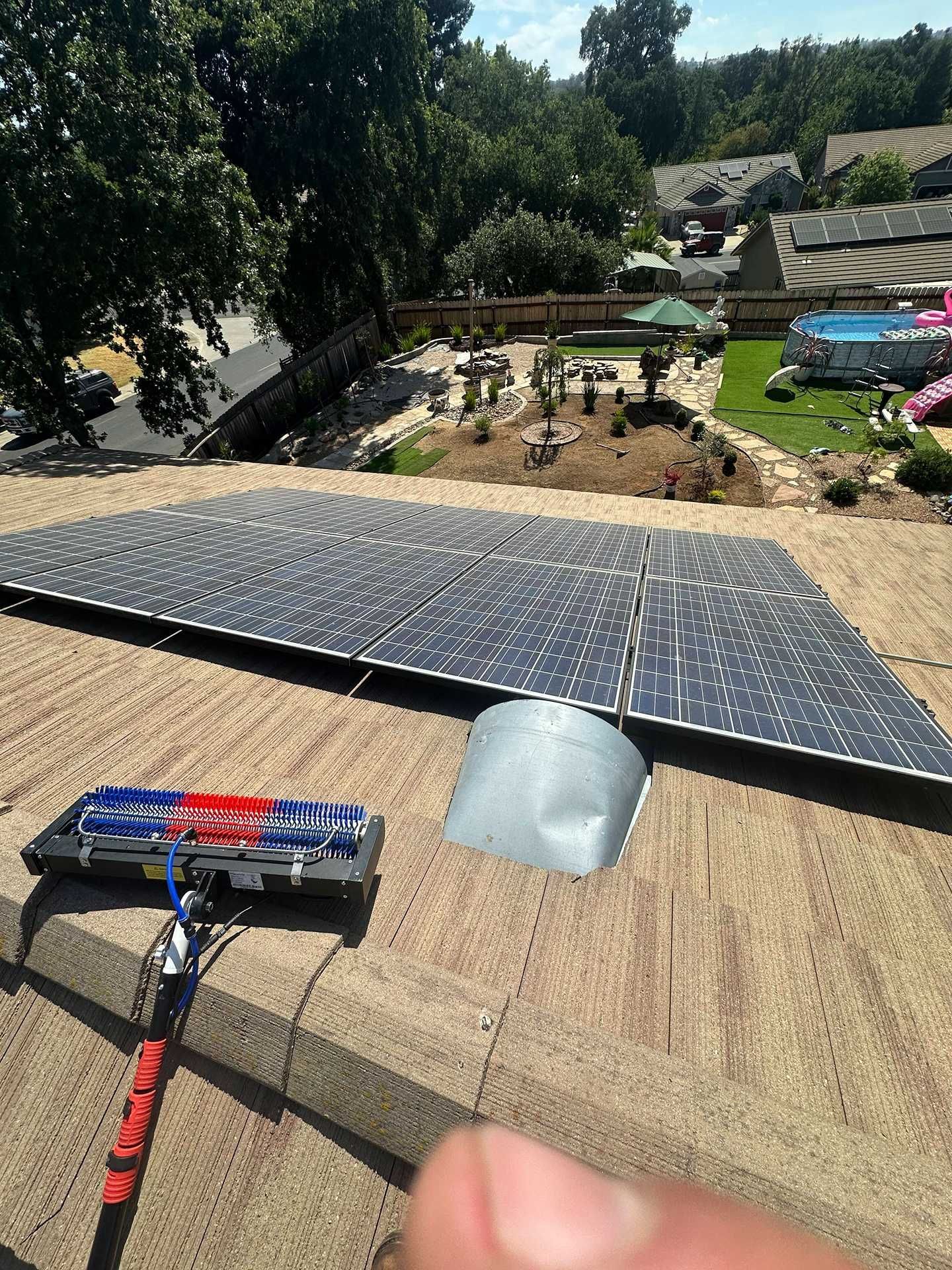 Solar panel array on a rooftop with tools in the foreground and a tree-lined neighborhood below.