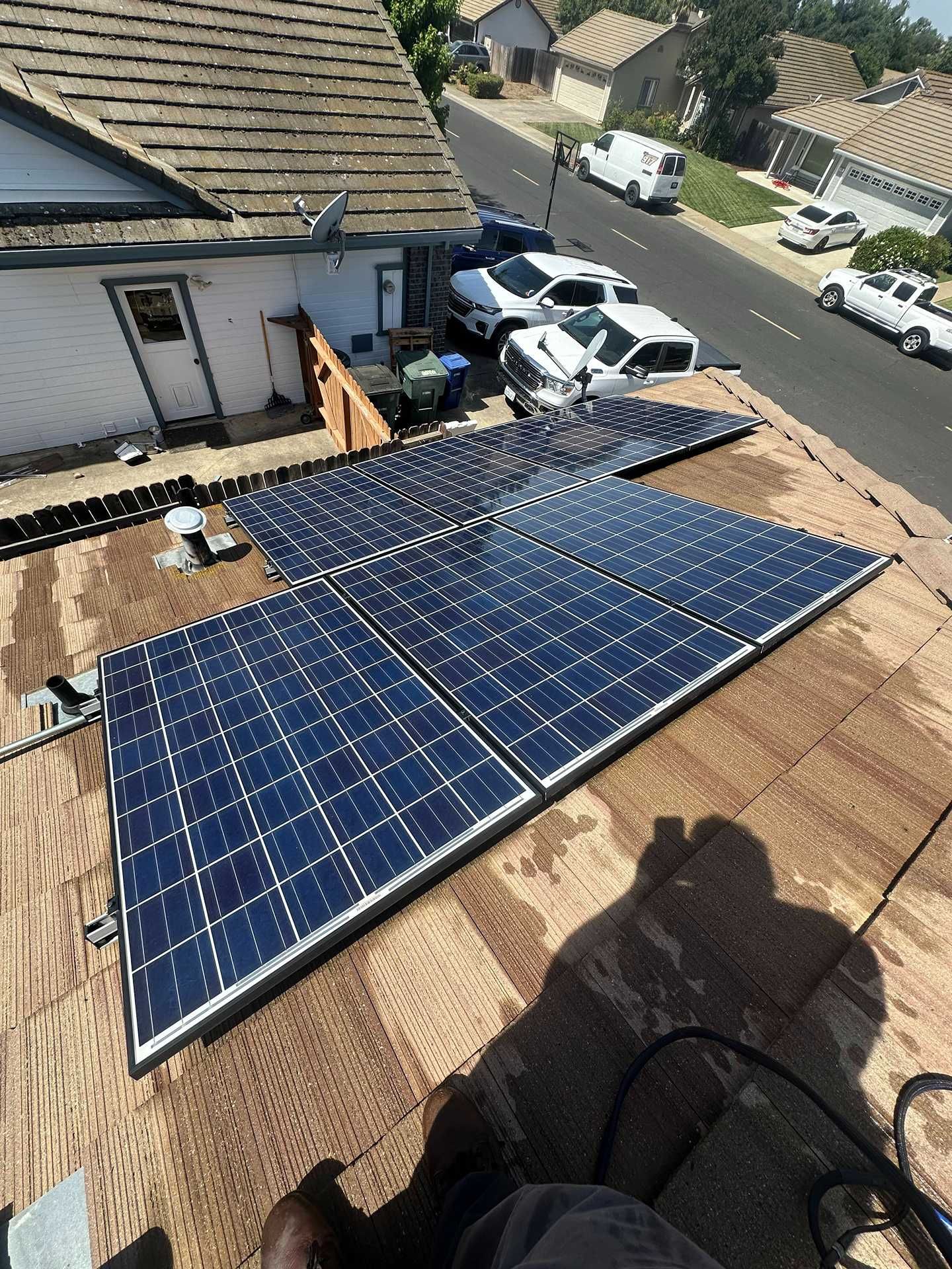 Solar panels mounted on a shingled roof, with rooftops and a street visible in the background.