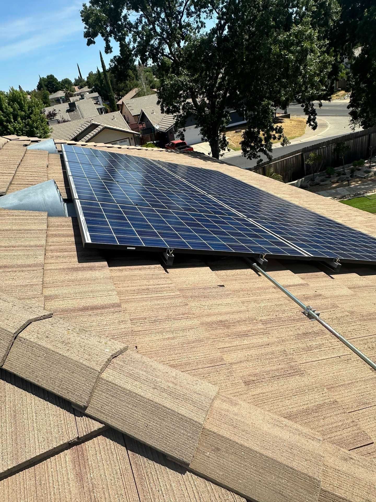 Solar panels mounted on a residential roof under a tree on a sunny day