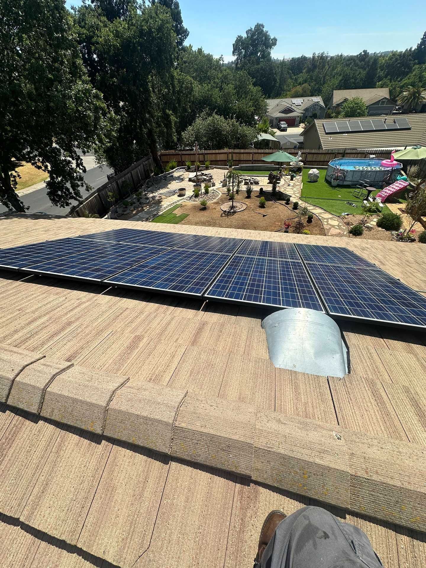 Solar panels on a rooftop overlooking a backyard with trees, garden beds, and a pool.
