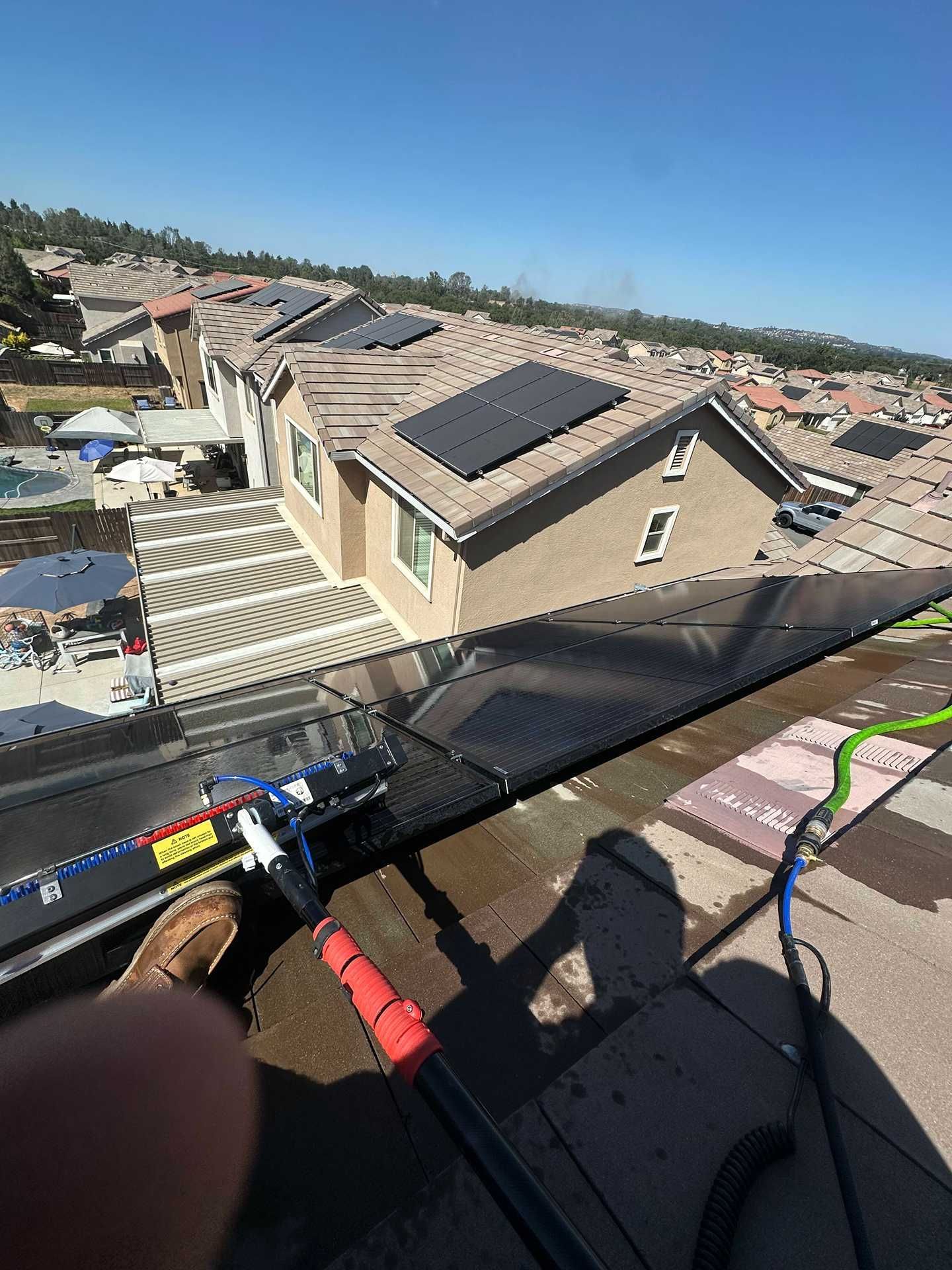 Roofer sealing a rooftop seam near solar panels on a residential house under a clear blue sky