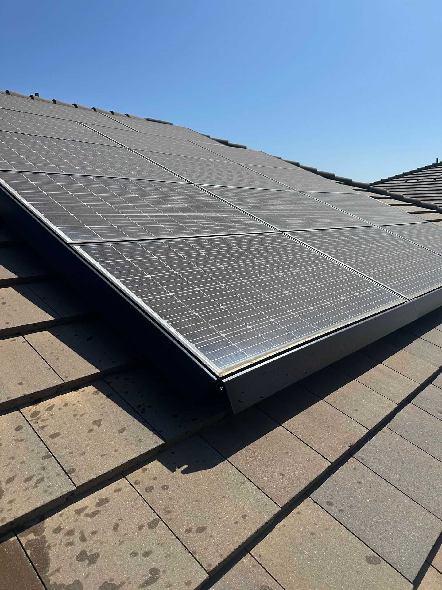 Solar panels mounted on a sloped residential roof under bright sunlight.