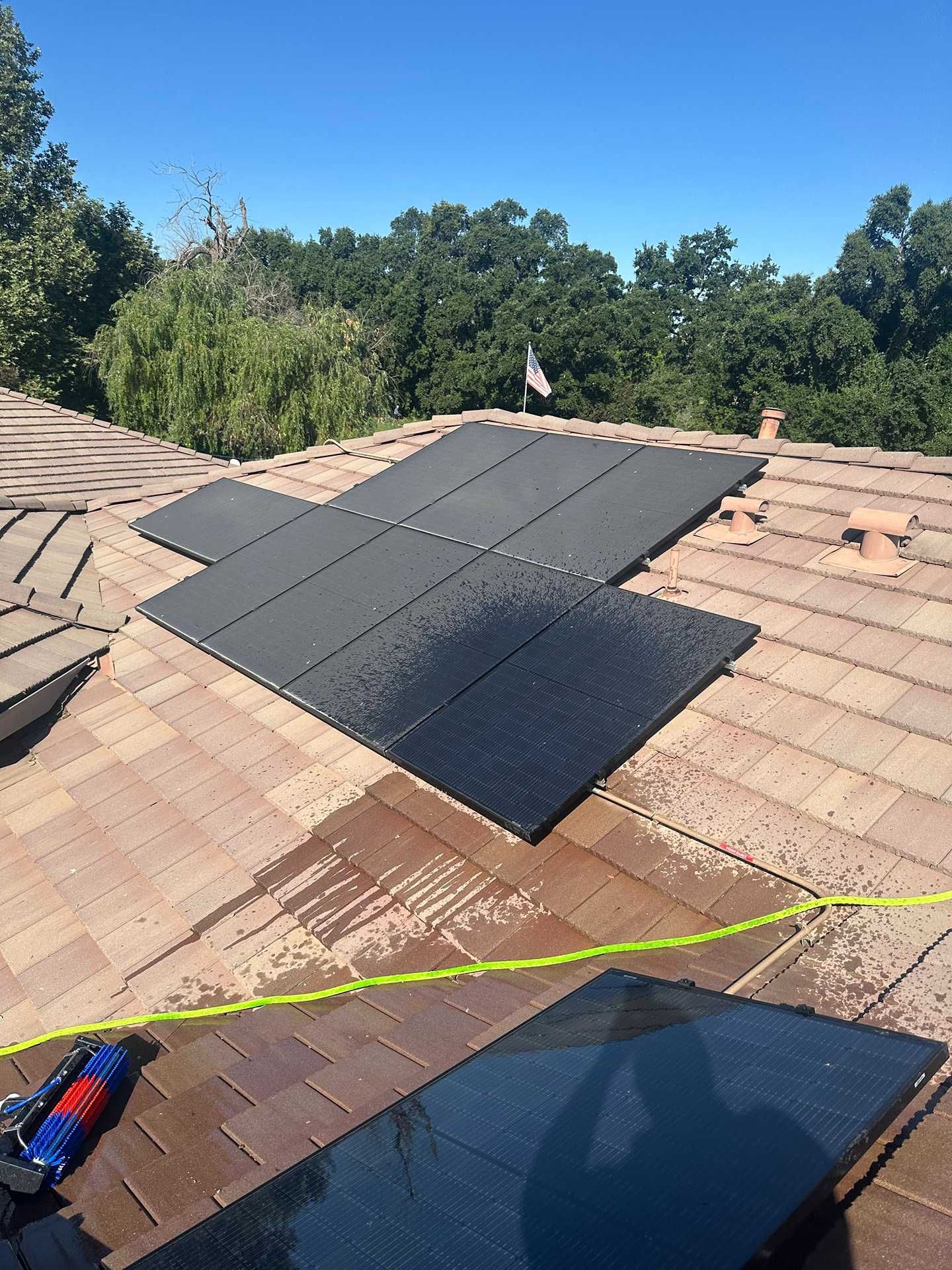 Solar panels installed on a shingled roof under a clear blue sky, with trees in the background.