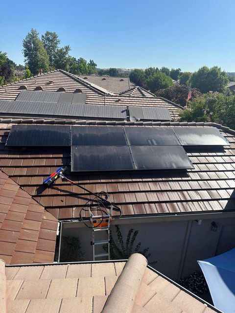 Rooftop solar panels on a shingled house, with a worker and tools near the edge.