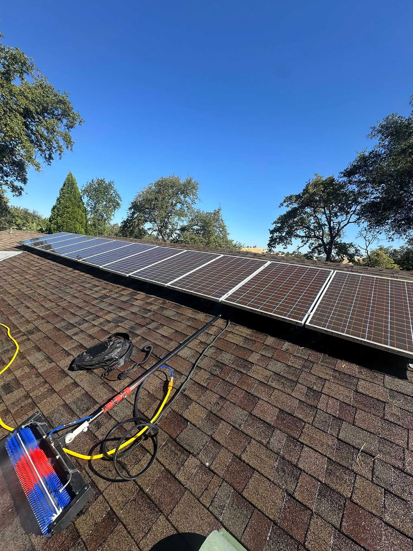 Solar panels being installed on a shingle roof under a clear blue sky.