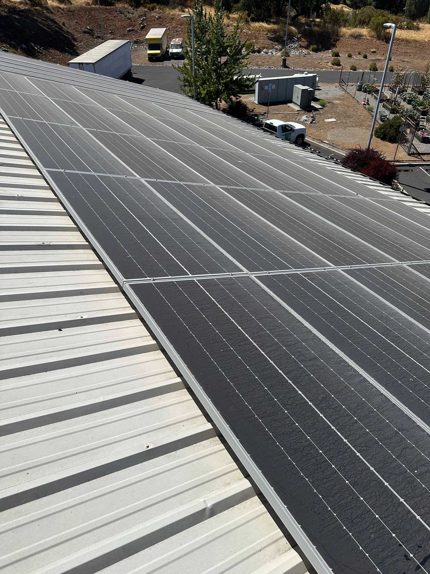 Solar panels installed on a sloped roof beside a white metal roof, with desert landscaping below.
