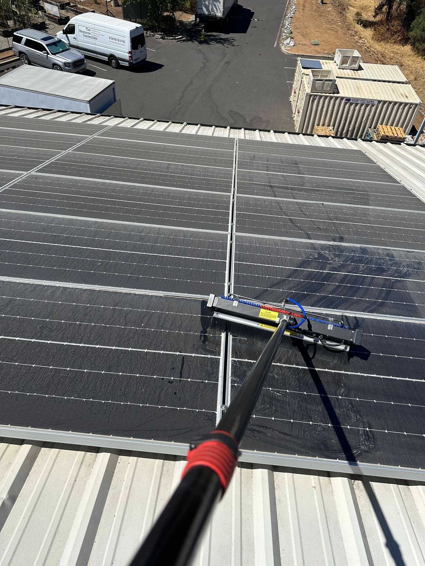 Solar panel roof being cleaned with a long-handled brush on an industrial rooftop.
