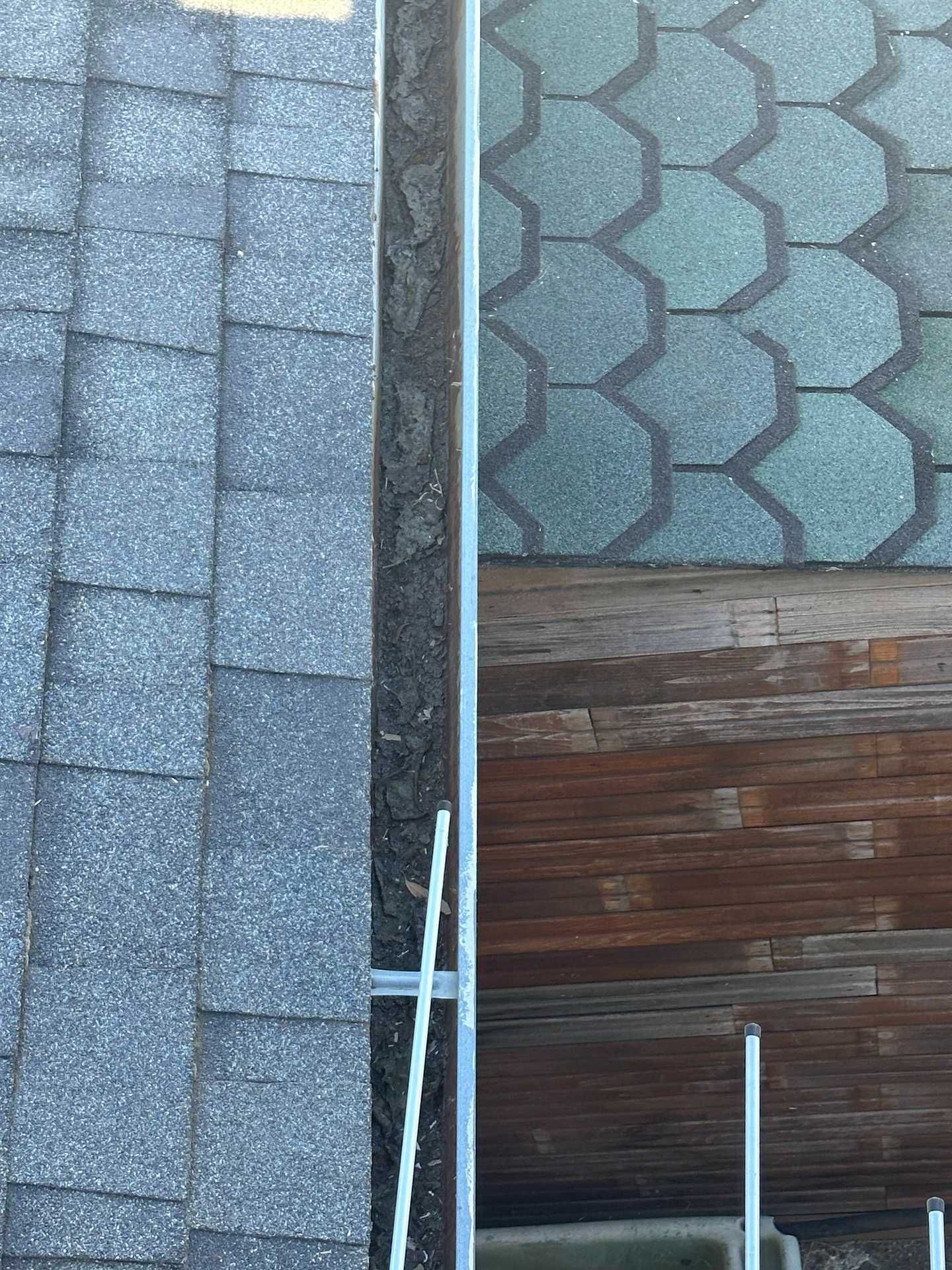 Roof shingles and siding meet at a narrow gap, with white pipes visible below.