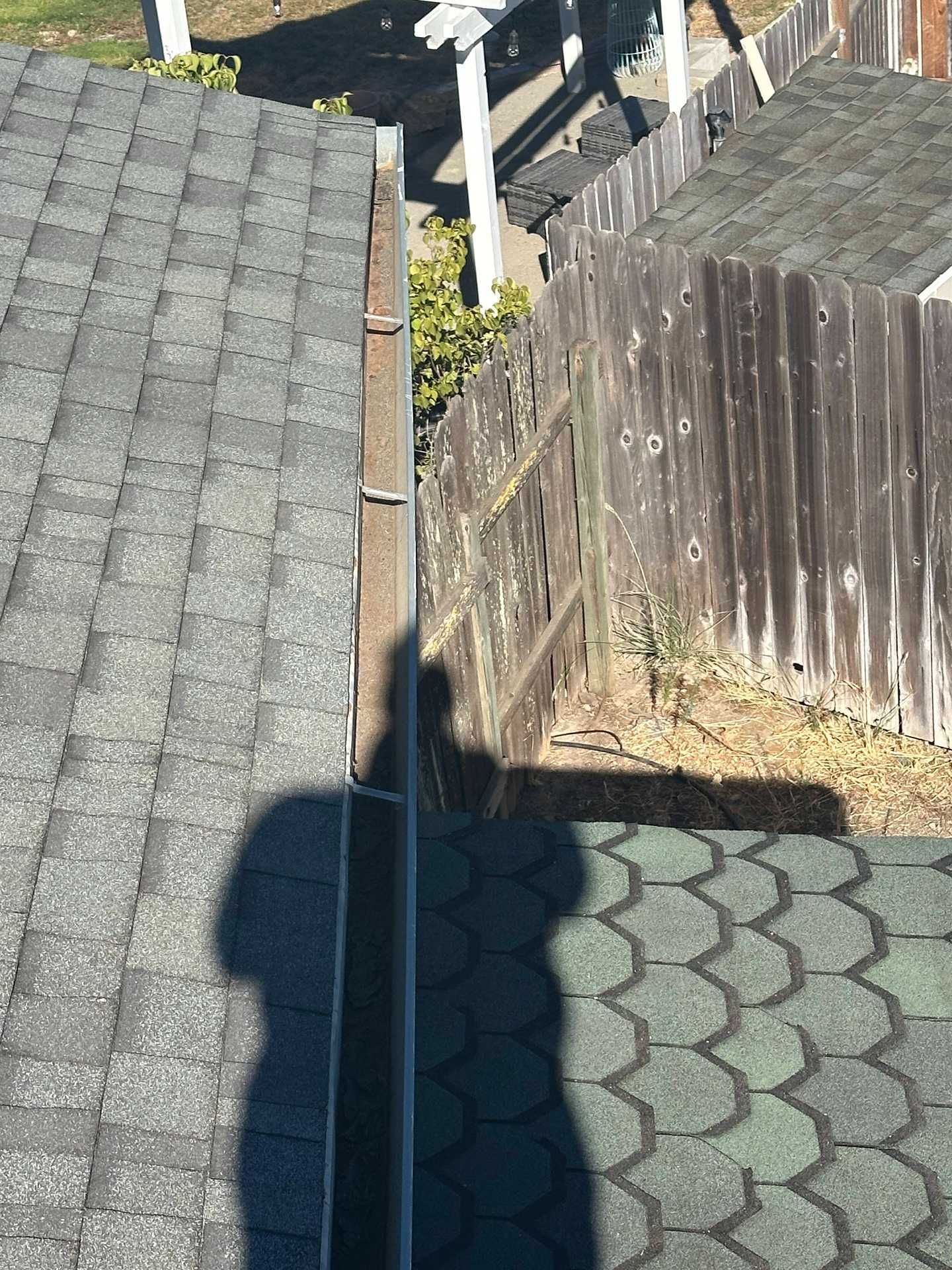 Rooftop and driveway view with solar panels, wooden fence, and a shadow in the foreground