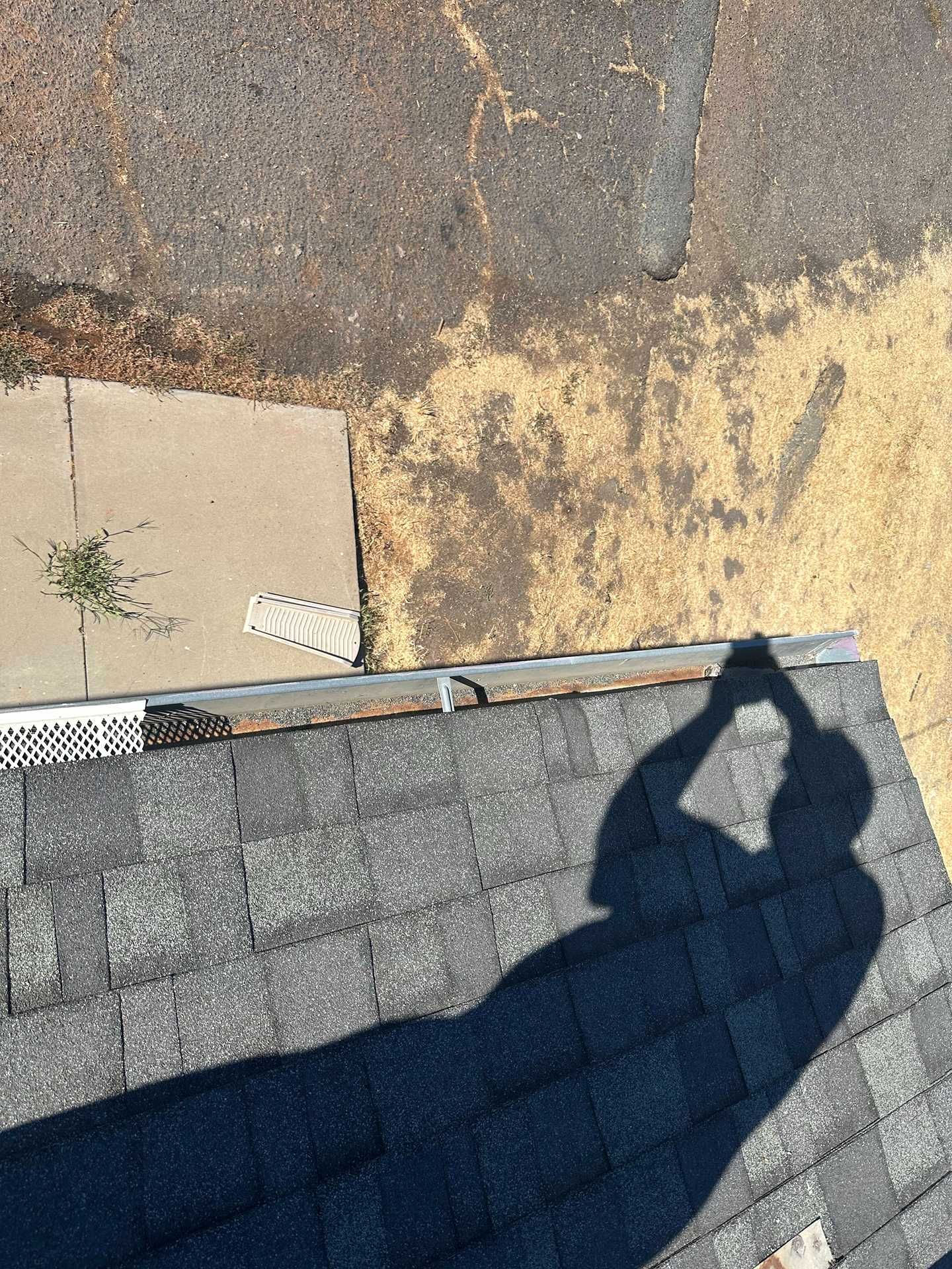 Roof edge with gray shingles beside a weathered concrete surface and a person's shadow