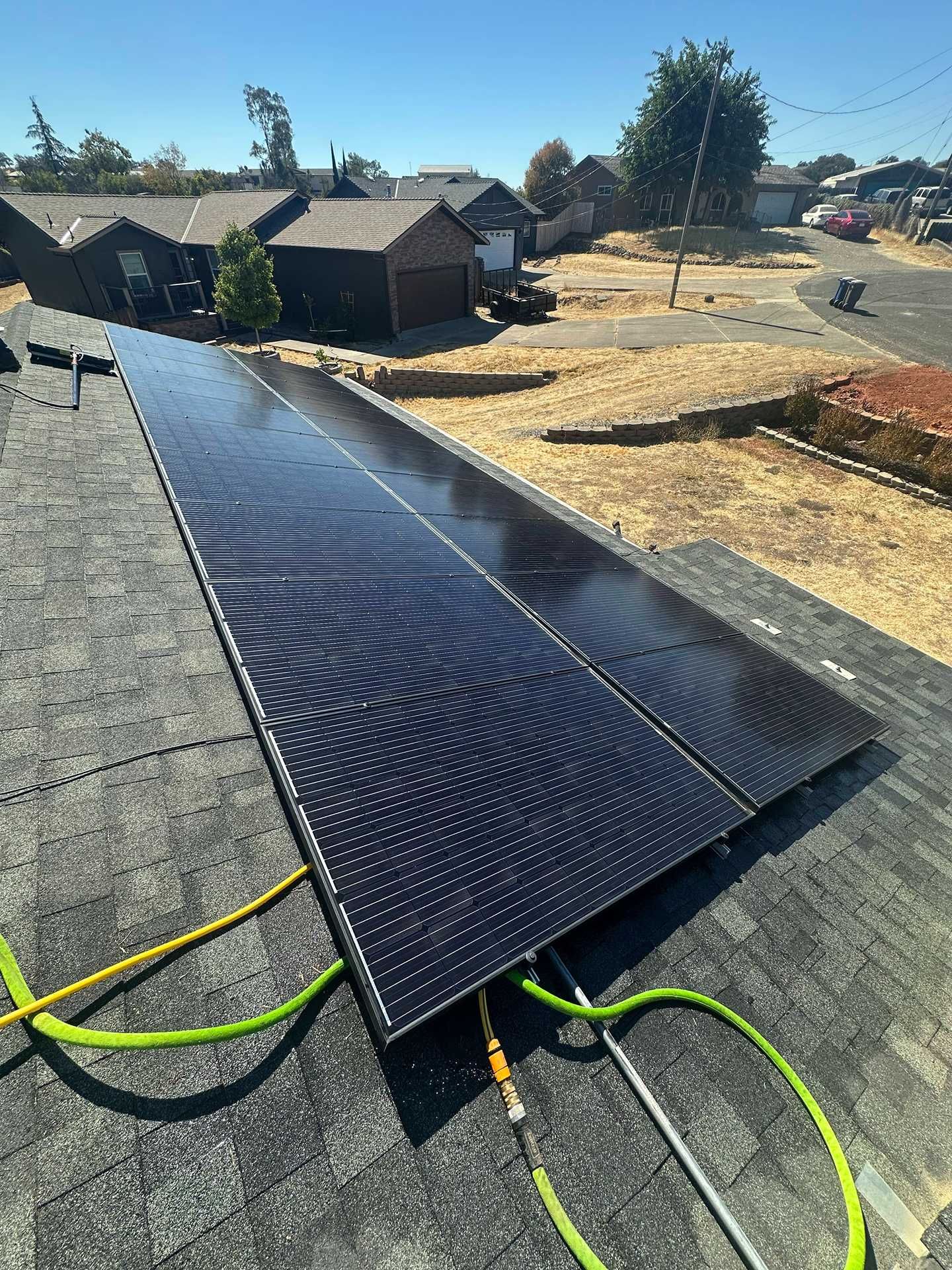 Solar panels laid on a rooftop, with a neighborhood and dry hillside in the background.