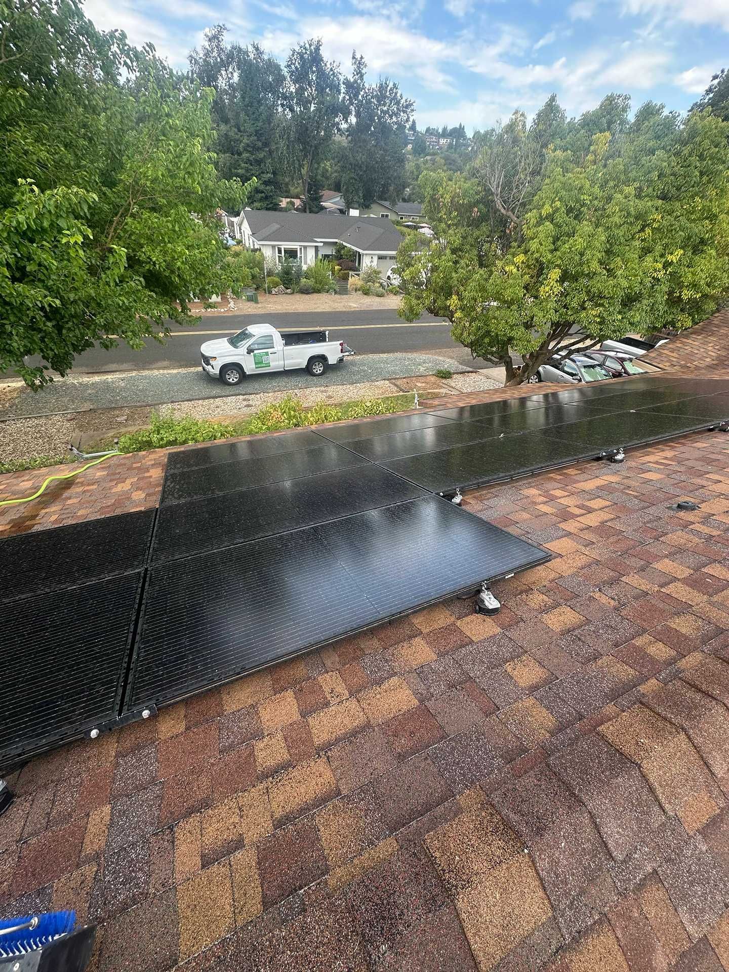 Rainy suburban street with a white pickup truck, trees, and a wet roof in the foreground