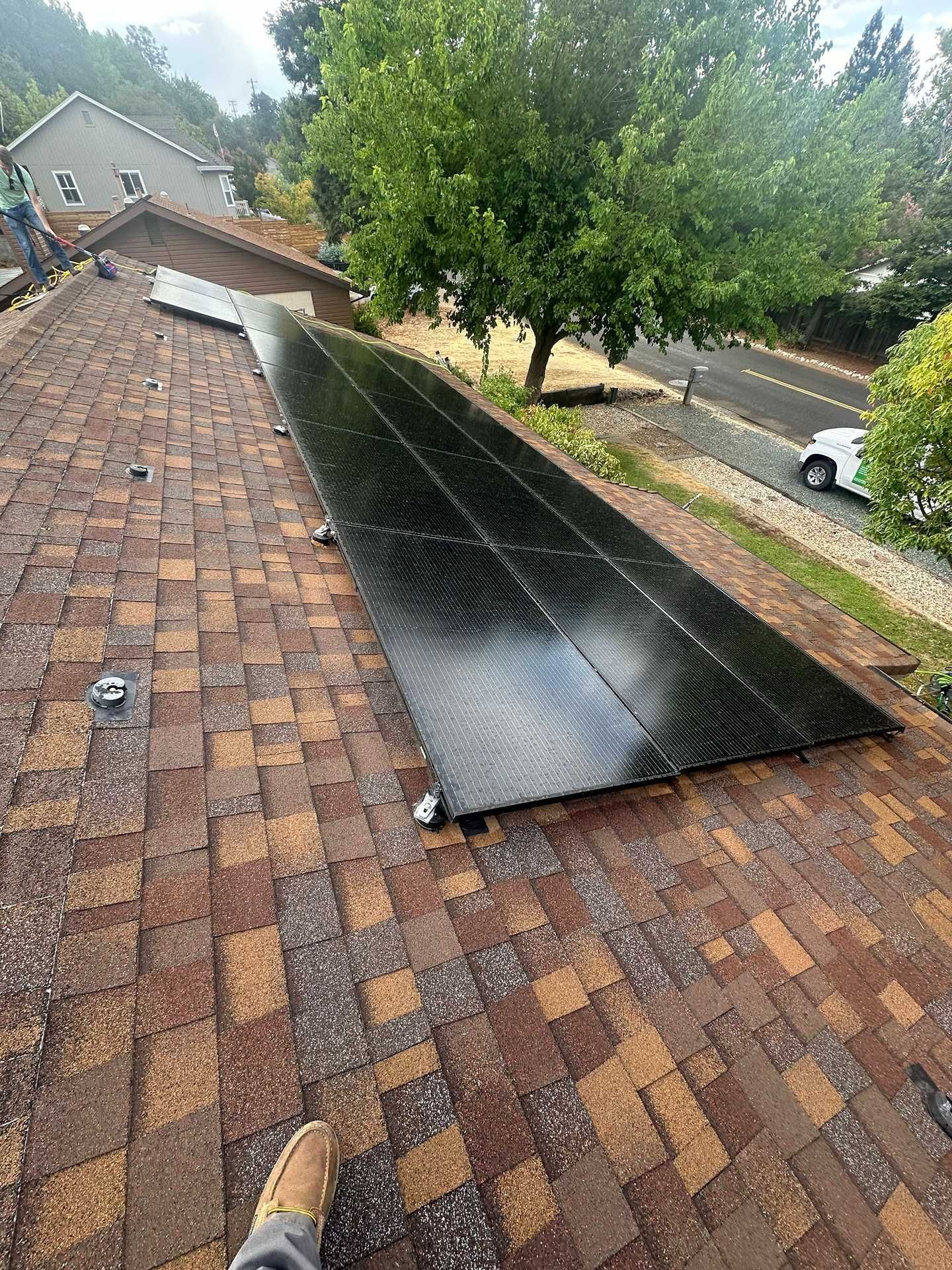 Solar panels installed on a shingled roof beside trees and a parked car