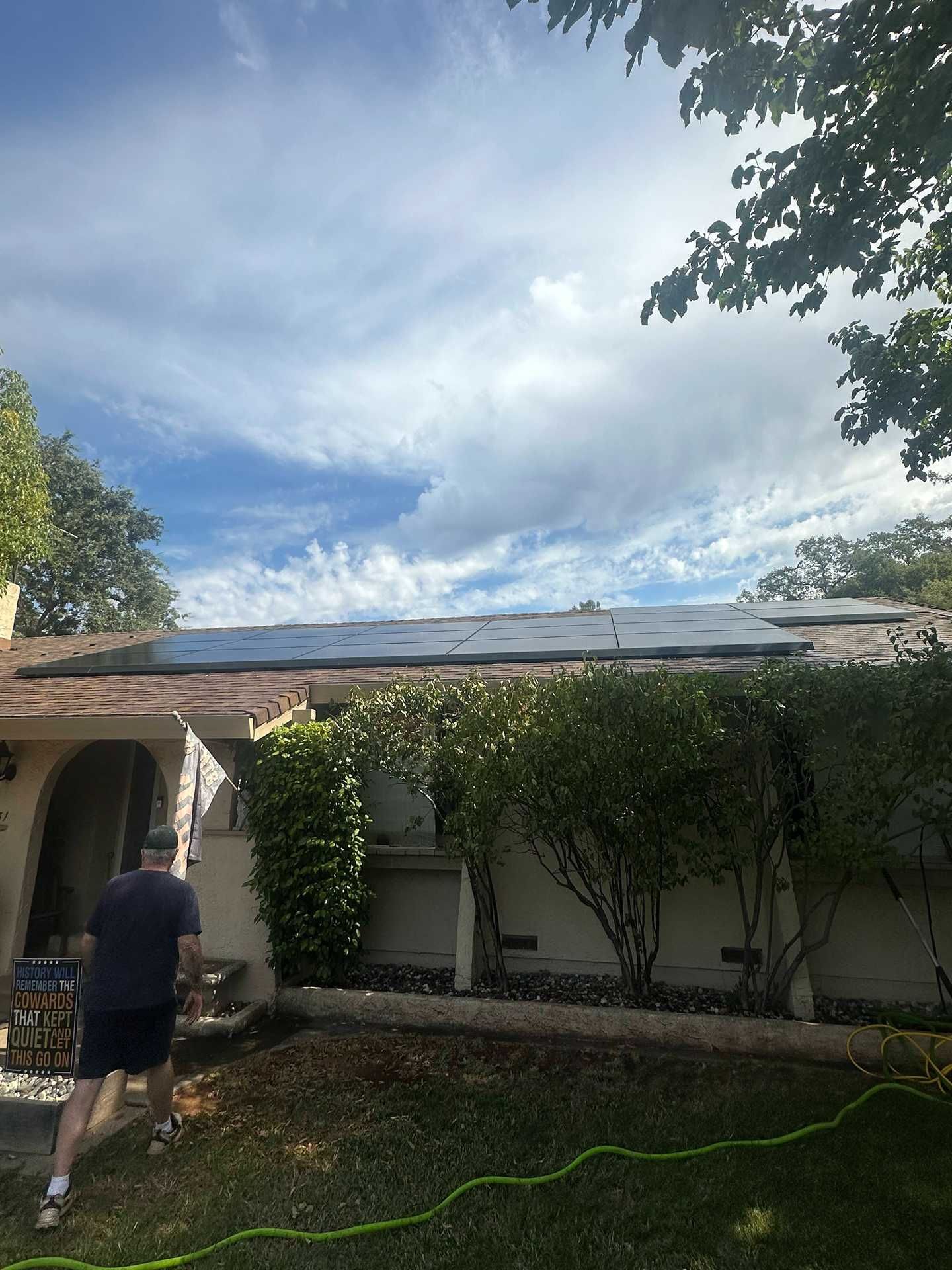 Person inspecting a house roof after storm damage, with a green hose in a backyard under cloudy sky.