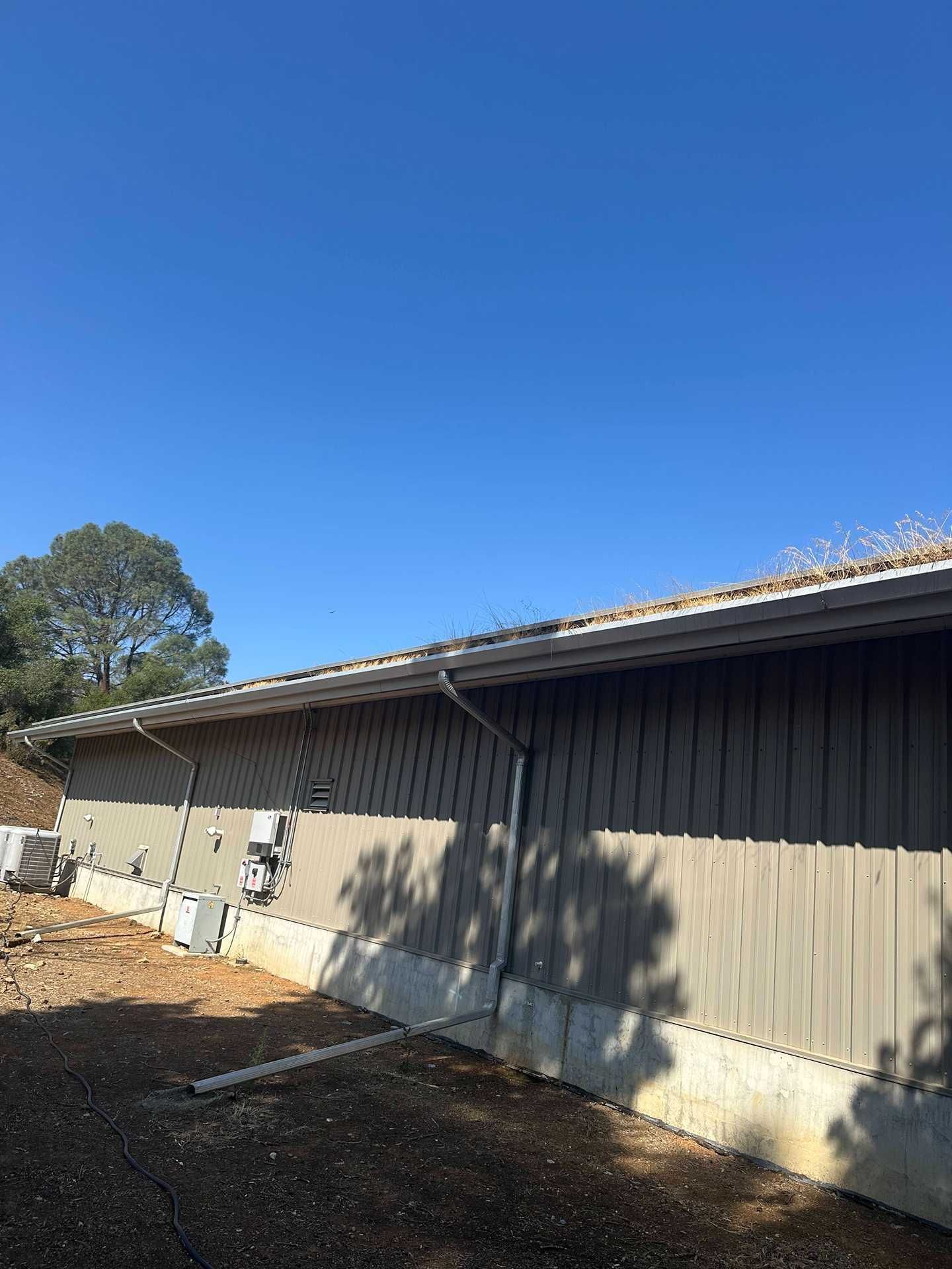 Side of a beige house with a sloped roof, gravel ground, and a clear blue sky.