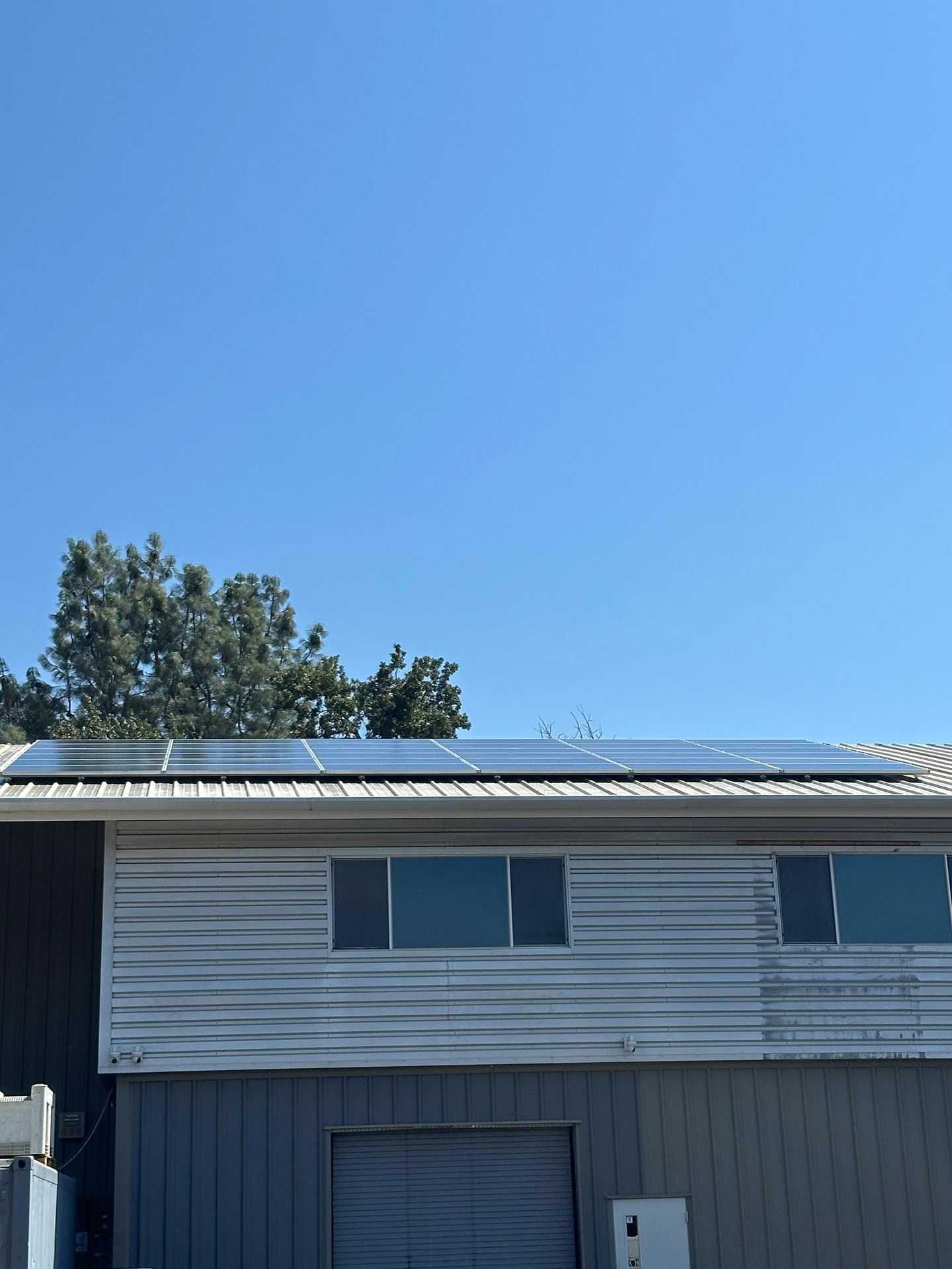 Blue two-story house with solar panels on the roof under a clear blue sky