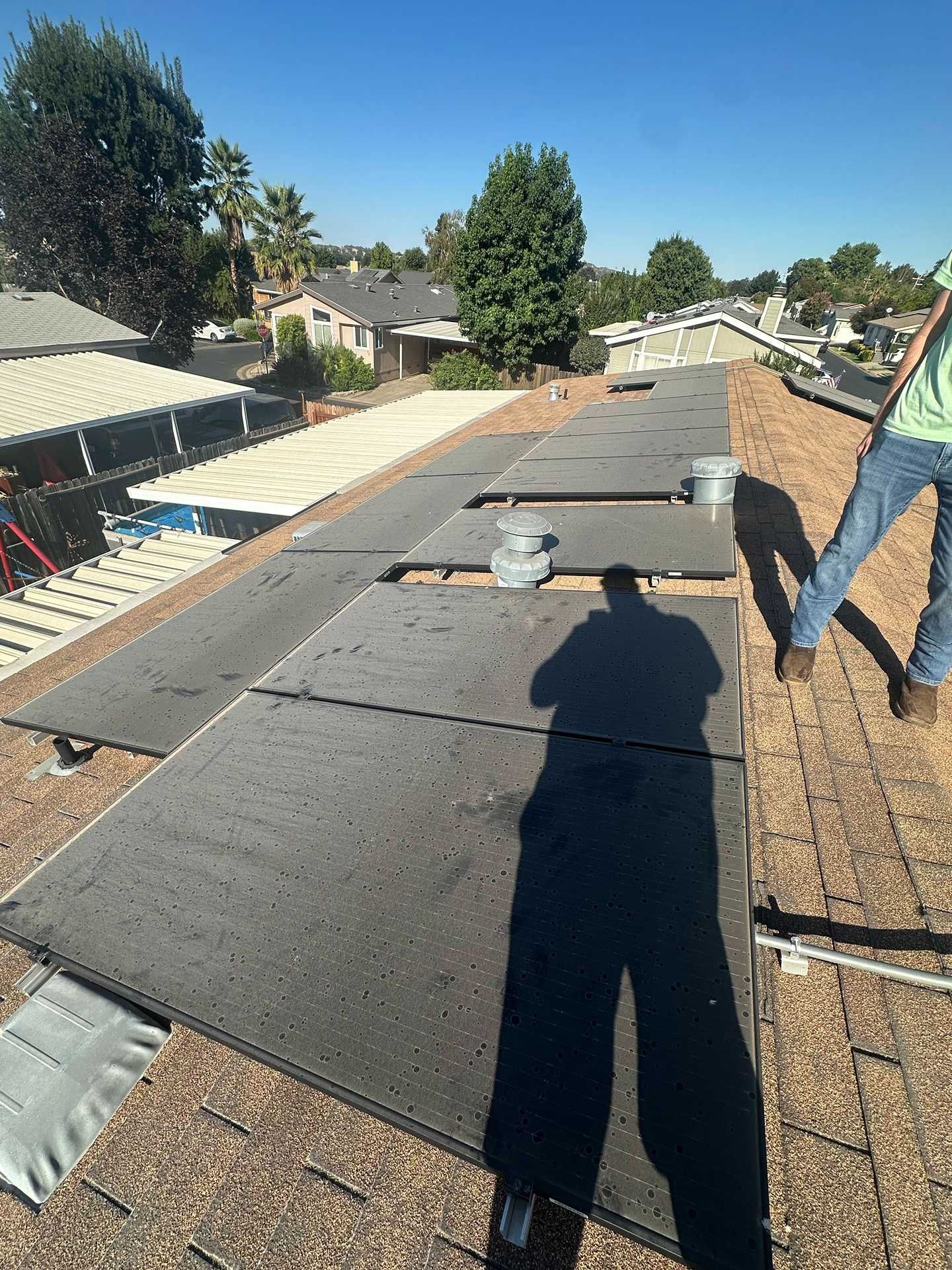 Rooftop under construction with roof panels, tools, and a worker’s shadow in bright daylight