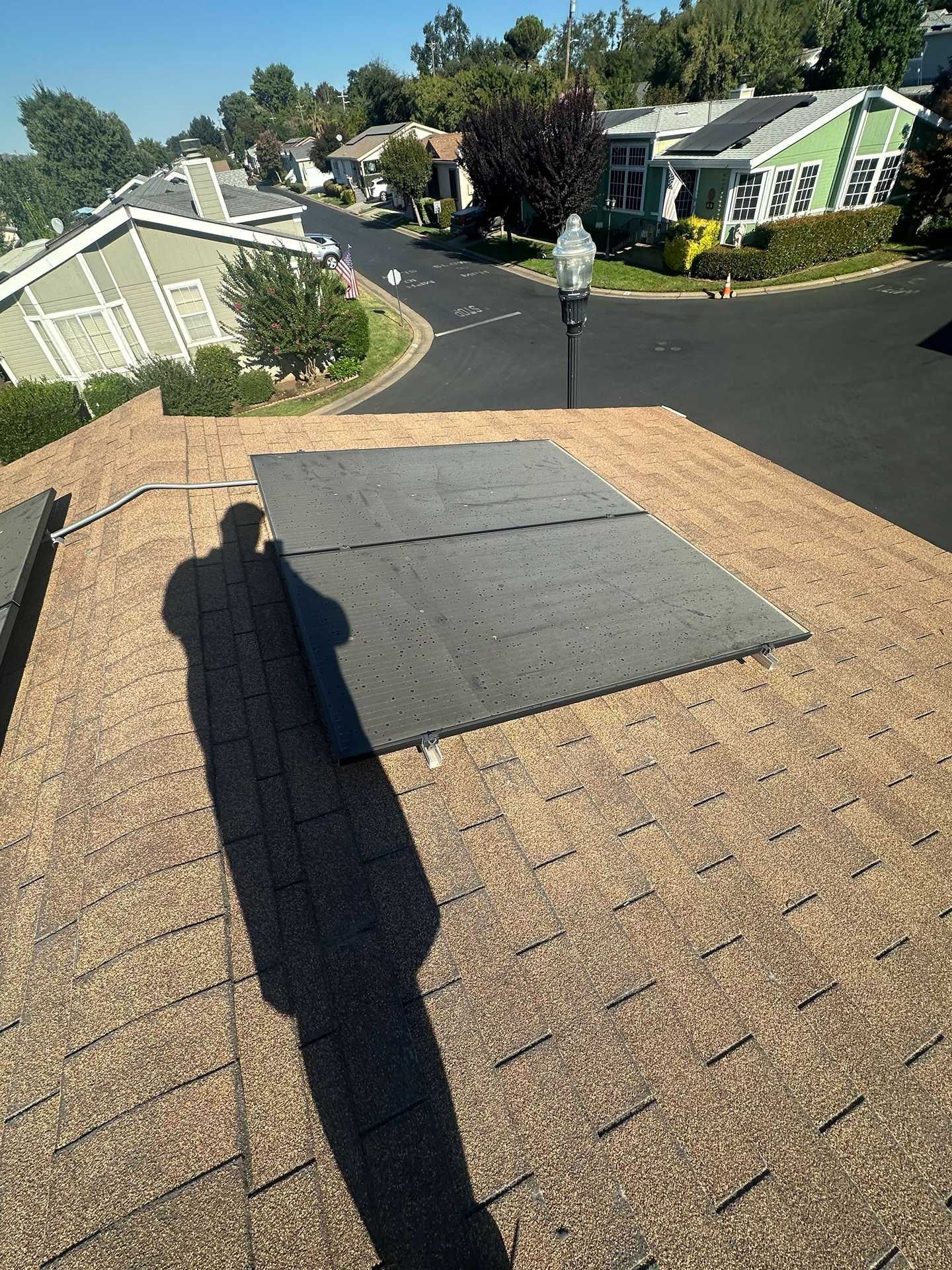 Rooftop view of a suburban street, with shingles, a roof hatch, and a shadow in the foreground.
