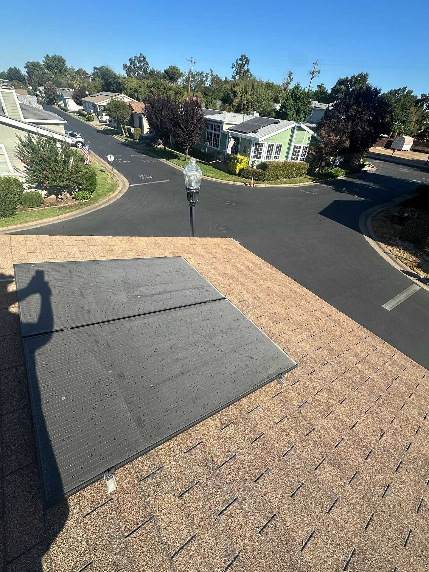 Roof shingles and black tar paper at the edge of a rooftop overlooking a suburban street.