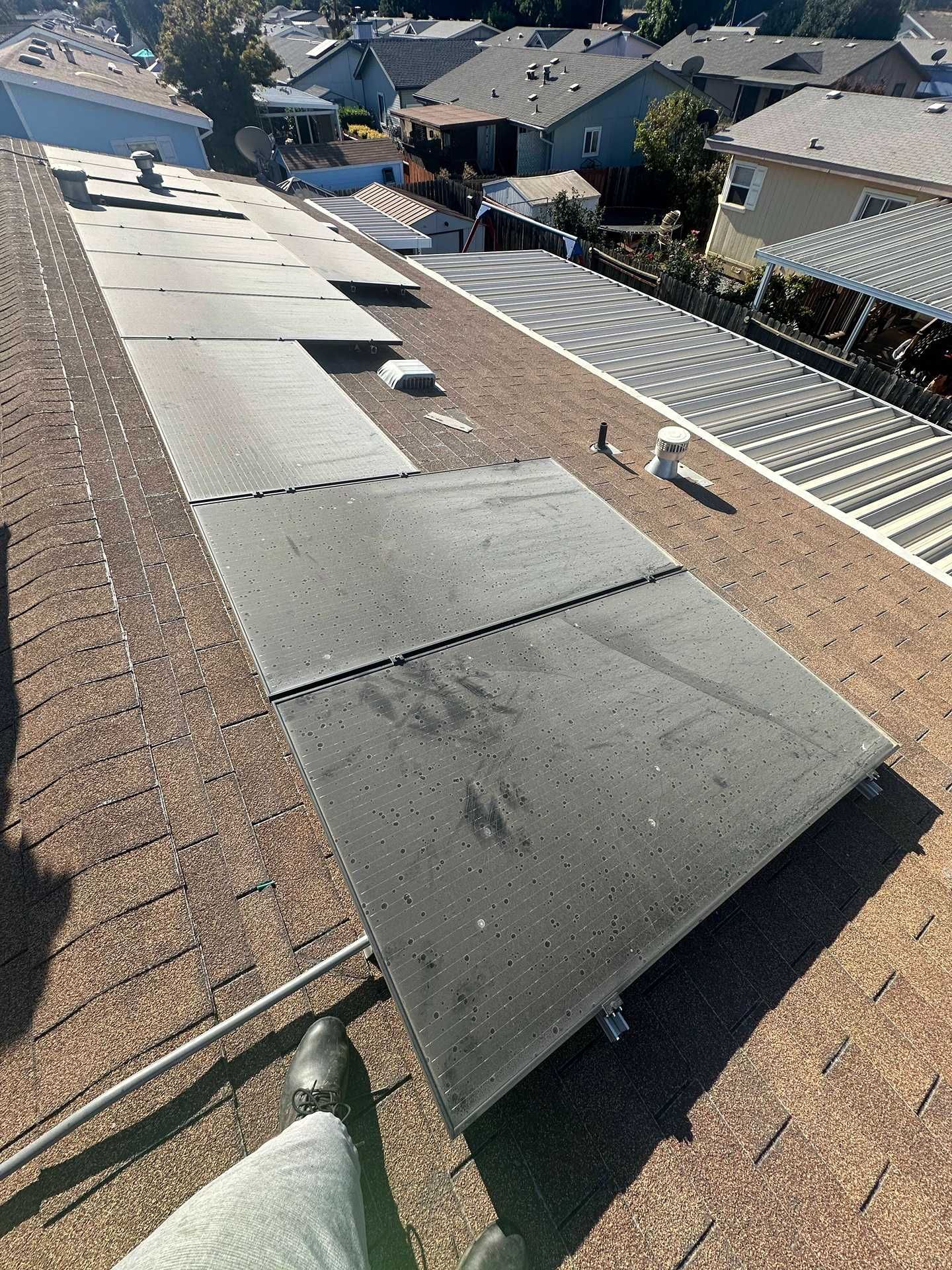 Roof under repair with rolled black roofing material on a sloped shingle roof near residential houses