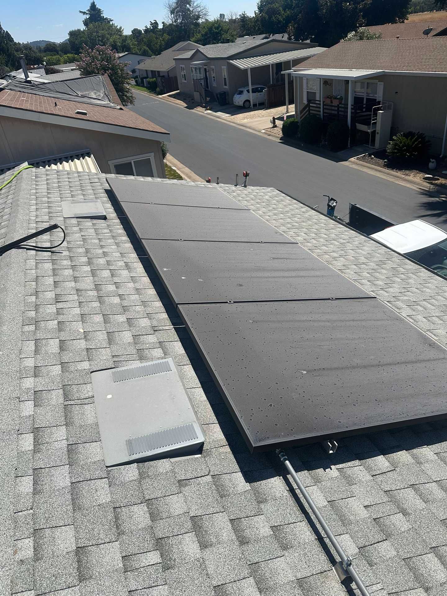 Rooftop with gray shingles and a dark solar panel overlooking a quiet residential neighborhood.